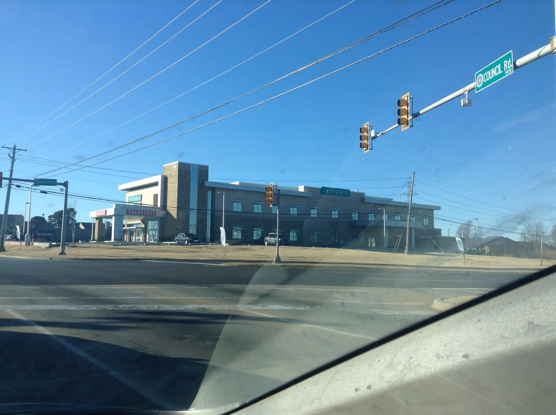 Wide view of a modern hospital exterior with emergency entrance and traffic intersection.