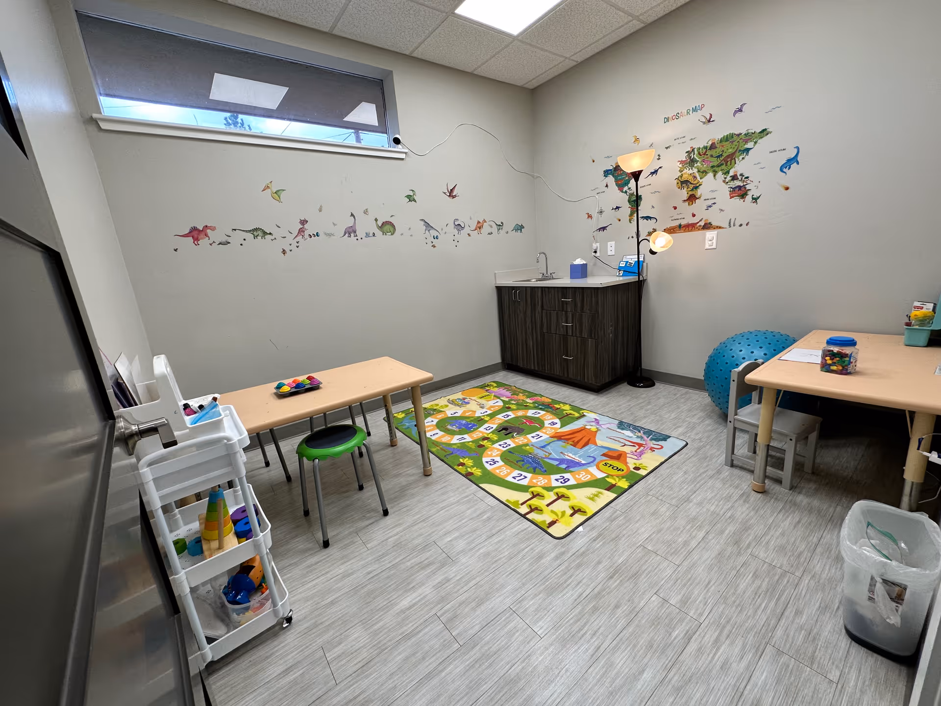 Child sized tables and a colorful dinosaur themed play area in an interior therapy room.
