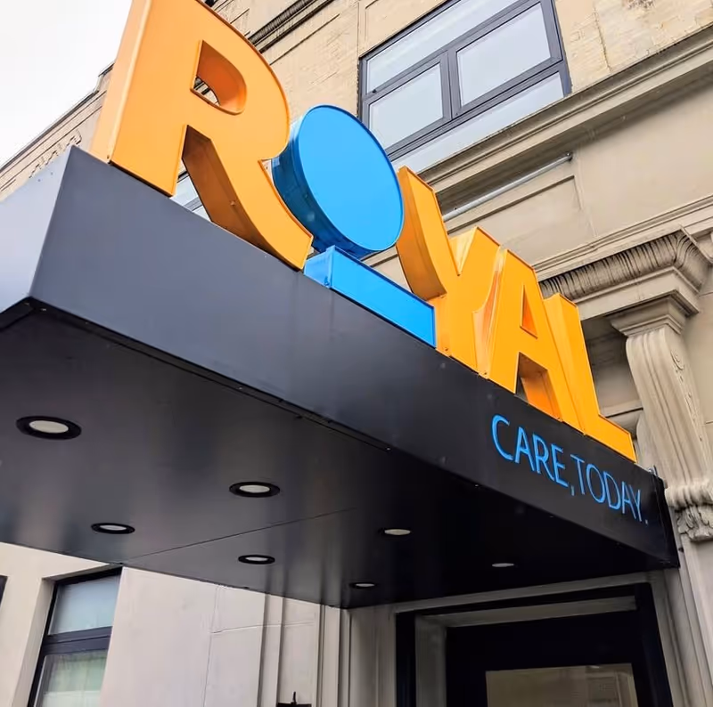 Close-up of the Royal Care exterior sign on a building front with orange and blue letters.
