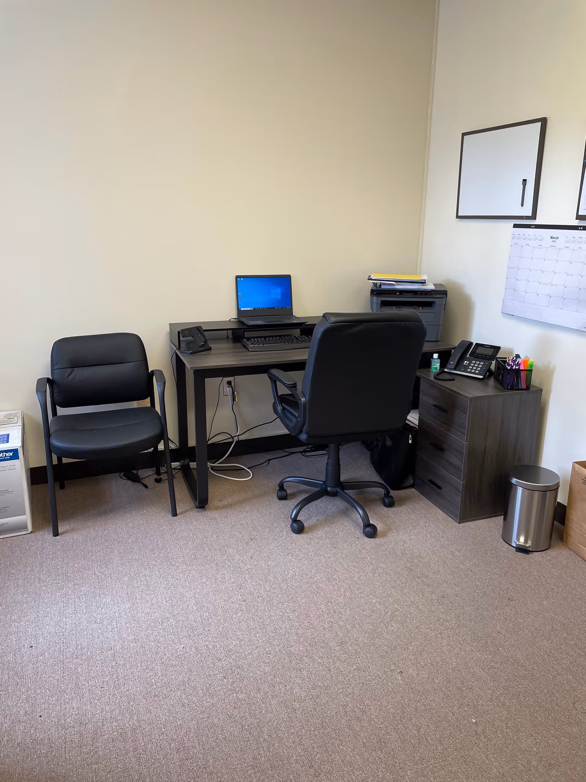 Small office with desk, computer, chair, and filing cabinet in a neutral room.
