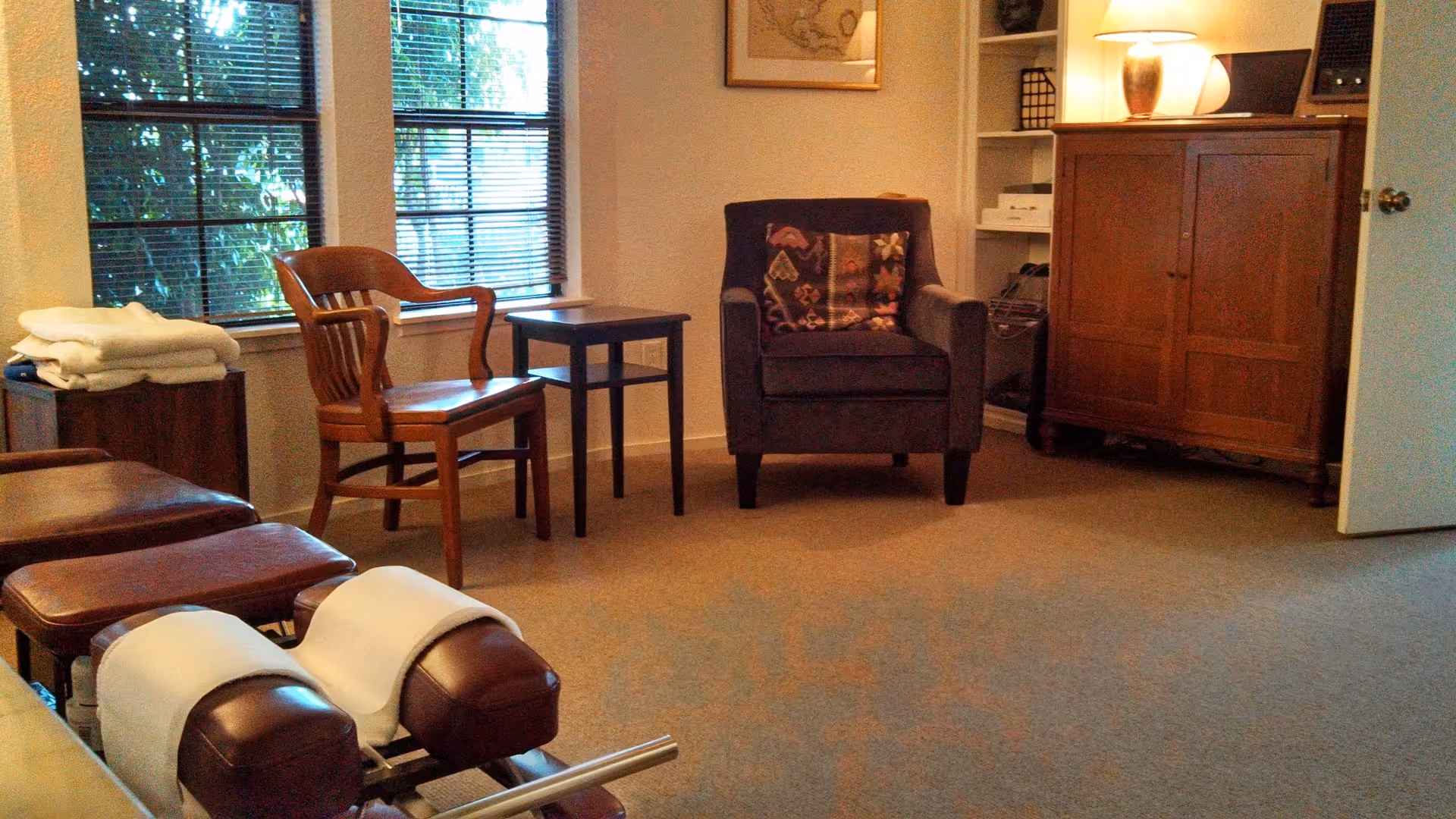 Senior living lounge with chairs, a recliner, cabinet, table, and large windows.
