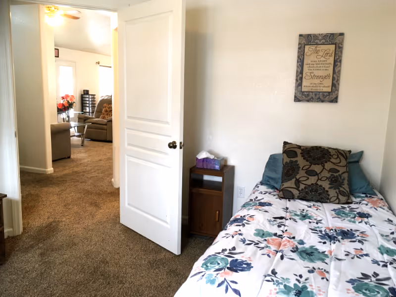 Bedroom with floral bedspread and pillows, opening to a living room.