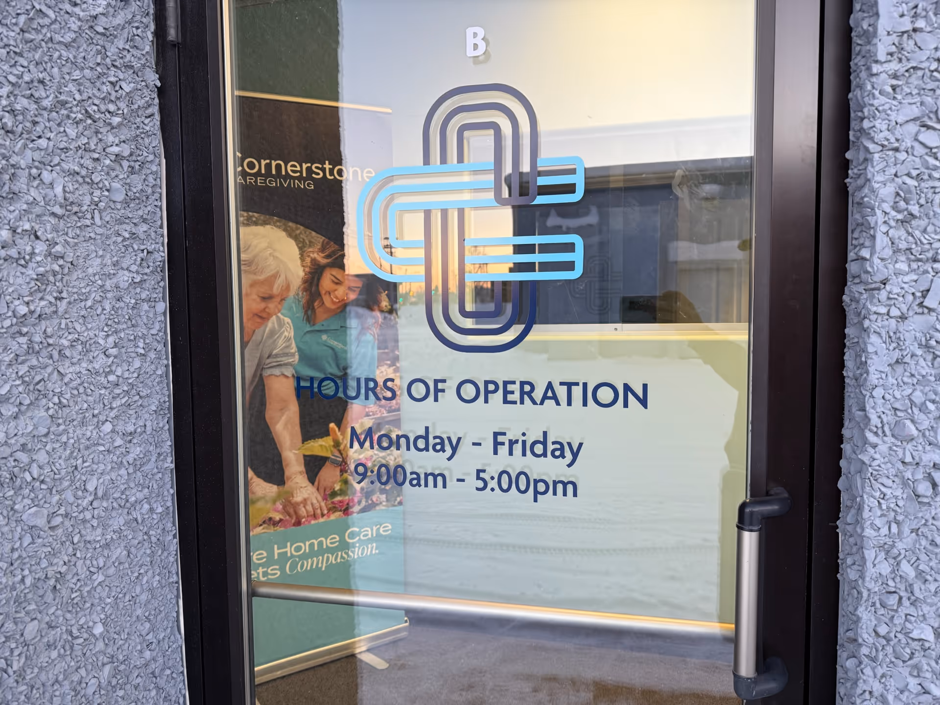 Glass door entrance with Cornerstone Caregiving logo and hours displayed on exterior wall.