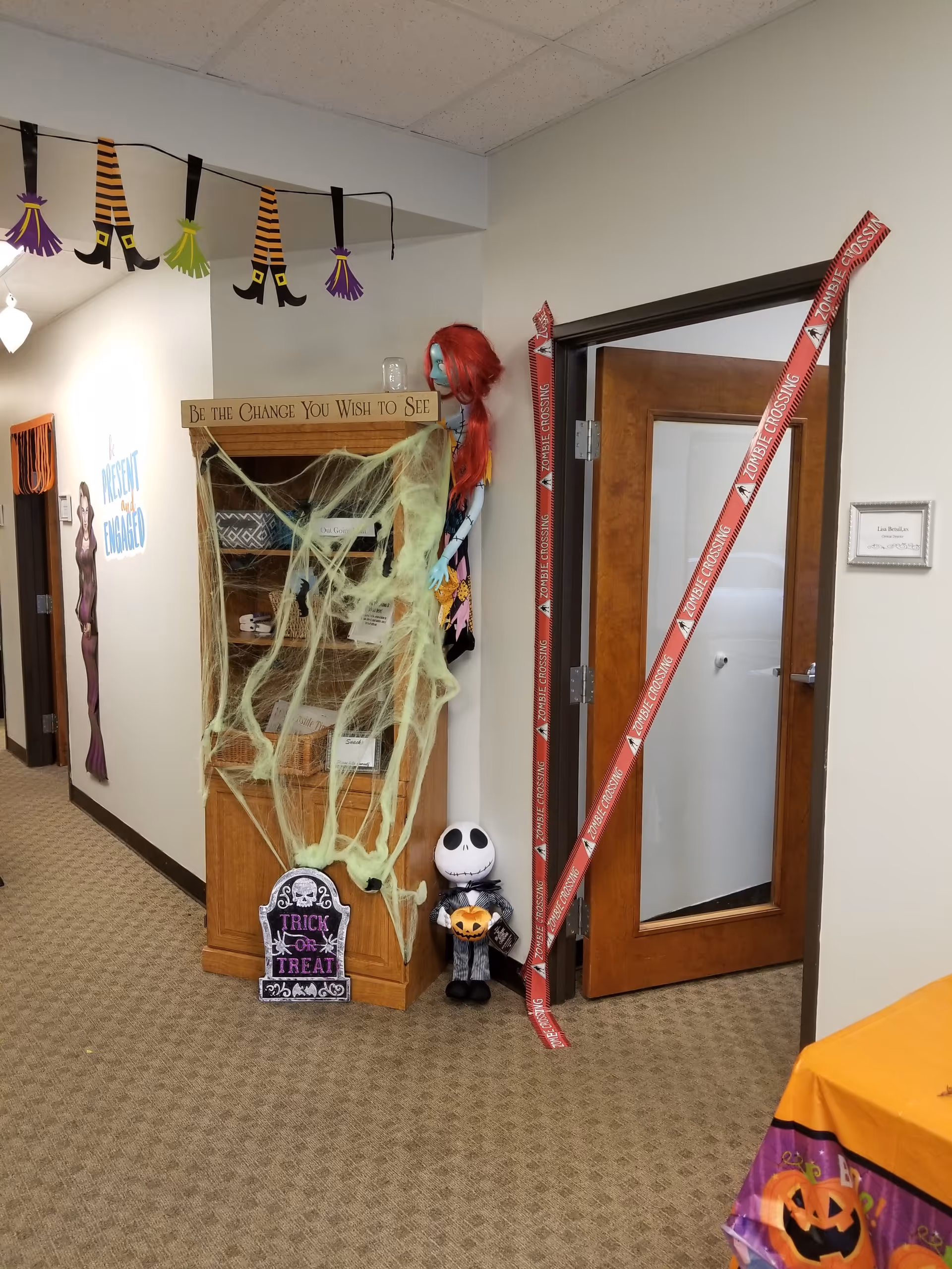 A hallway in a senior facility decorated for Halloween with cobwebs, pumpkins, and costumes.