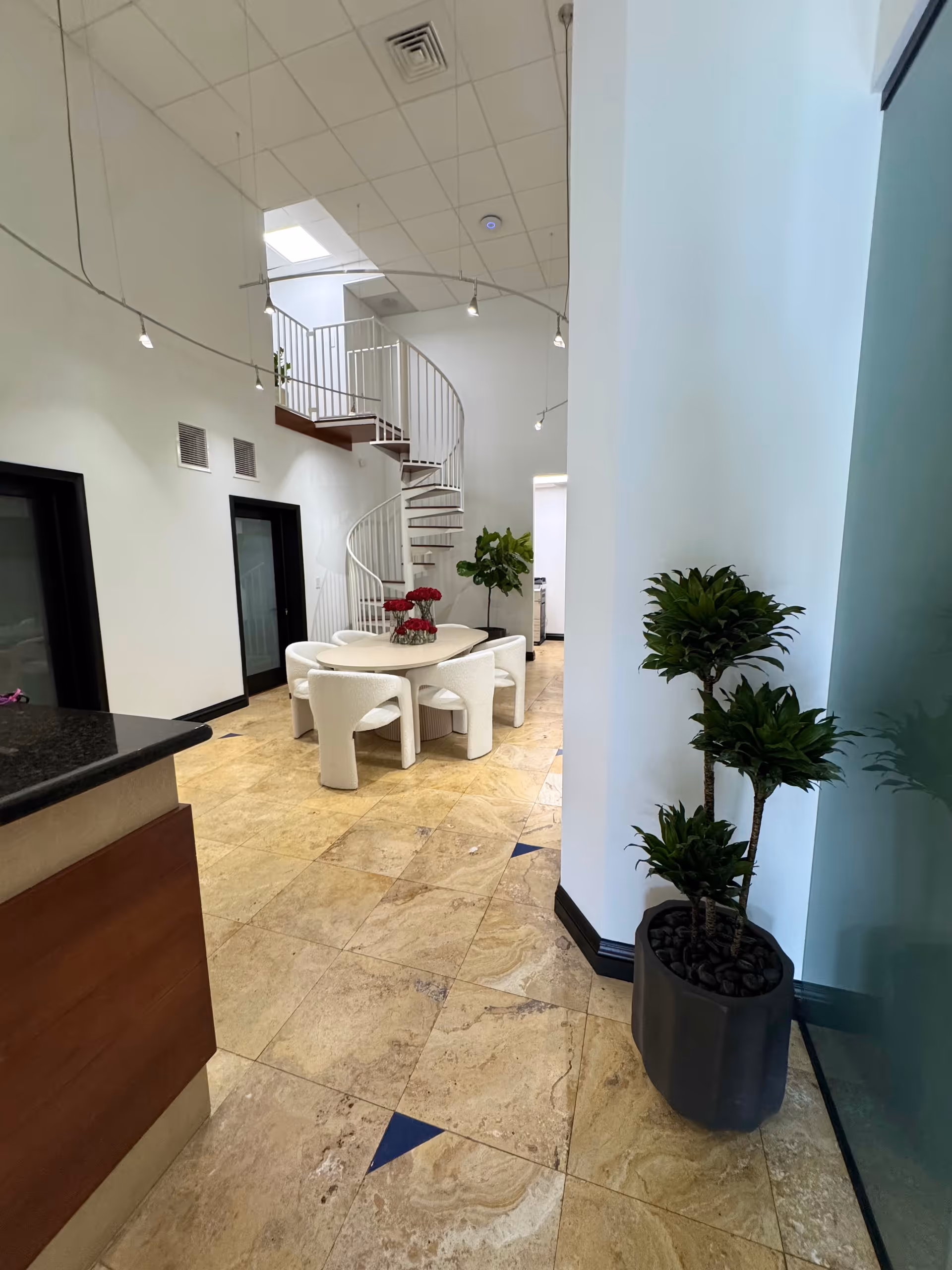 Bright interior lobby with spiral staircase, round dining table, white chairs, and potted plants.