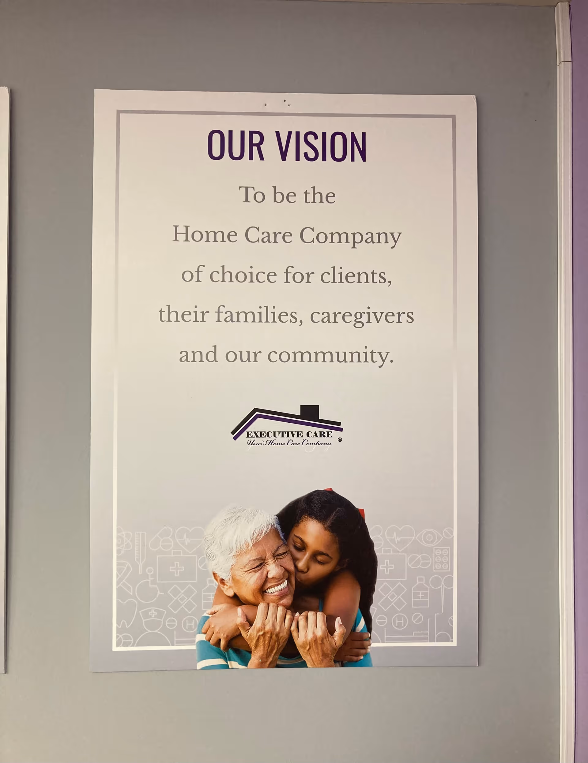 Poster on wall shows Our Vision text and image of caregiver embracing elderly woman.