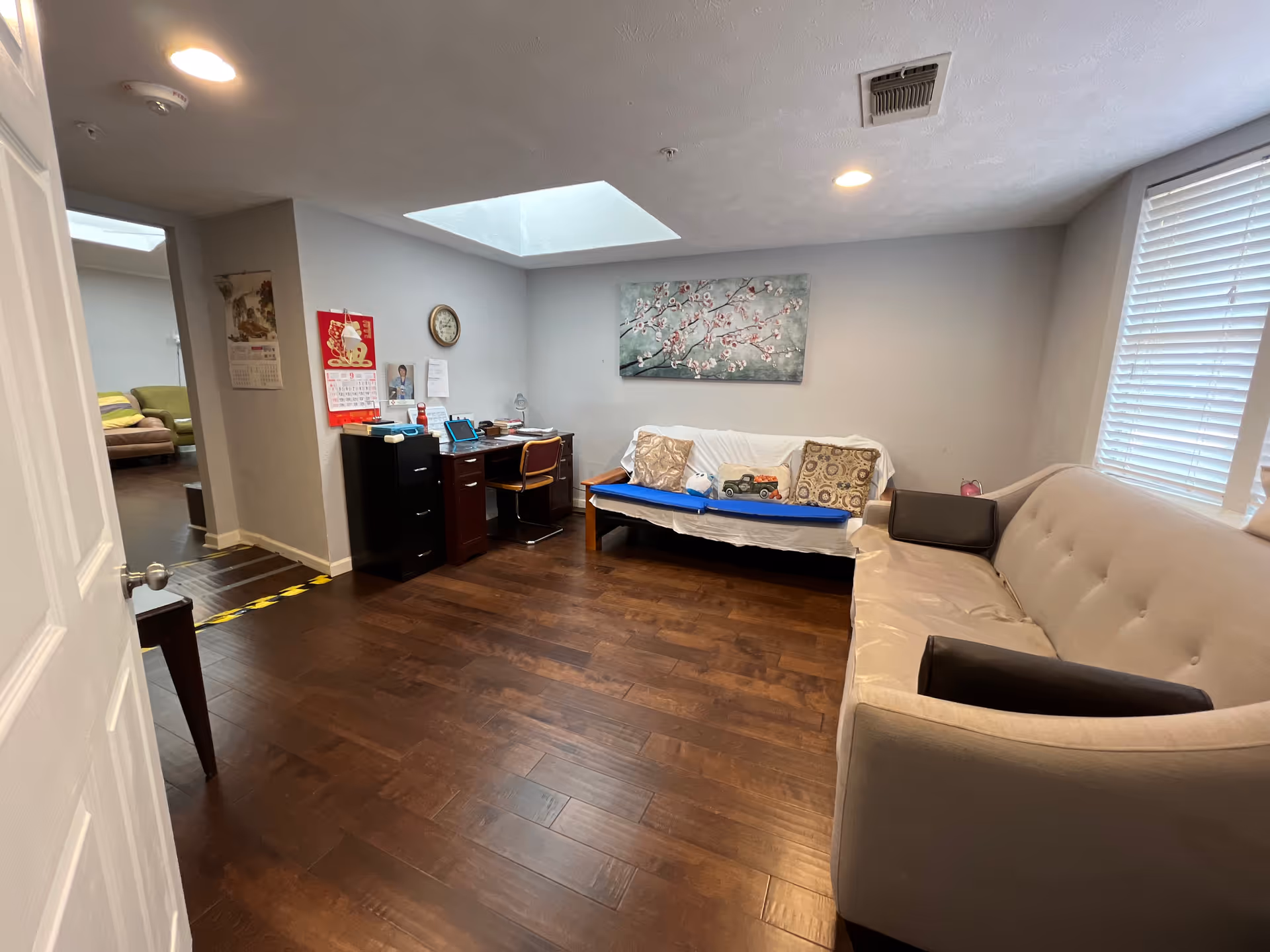 Cozy common living area with beige sofas, wood floors, desk, and wall art.