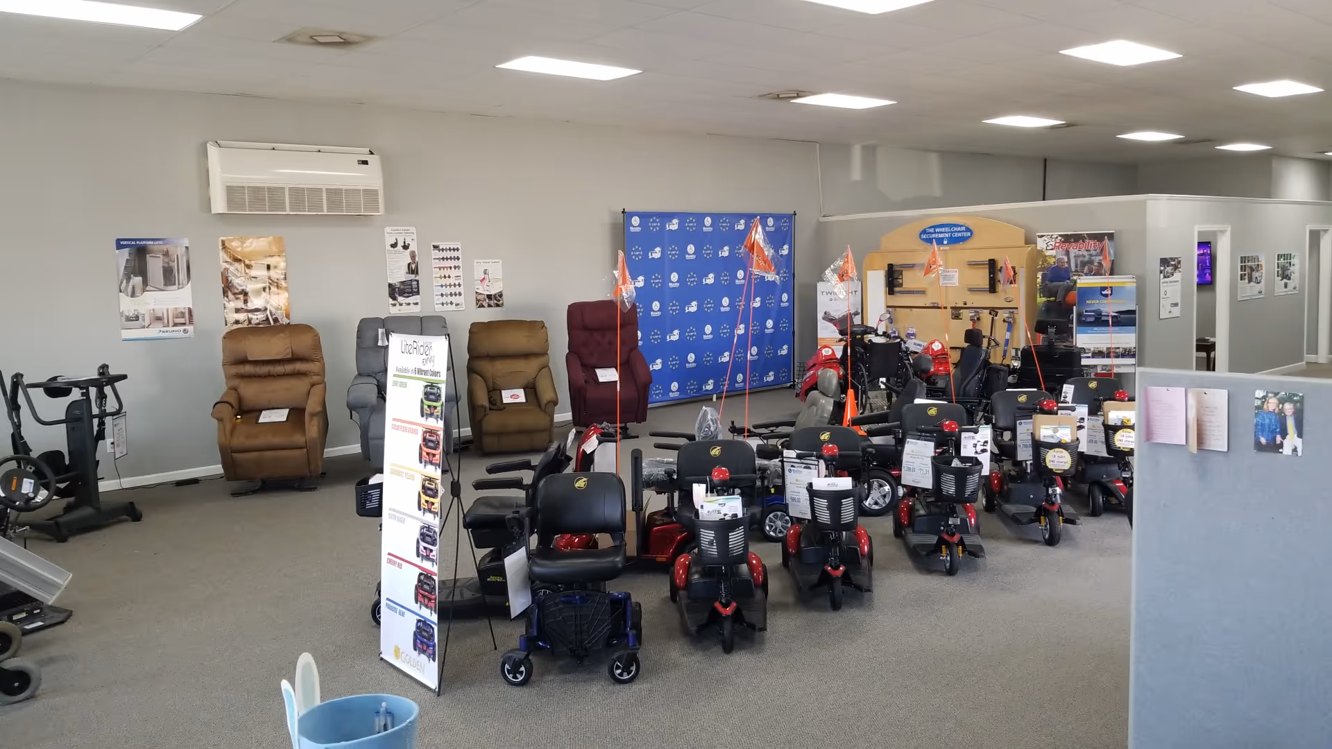 Indoor showroom with numerous mobility scooters and reclining chairs, walls lined with posters.