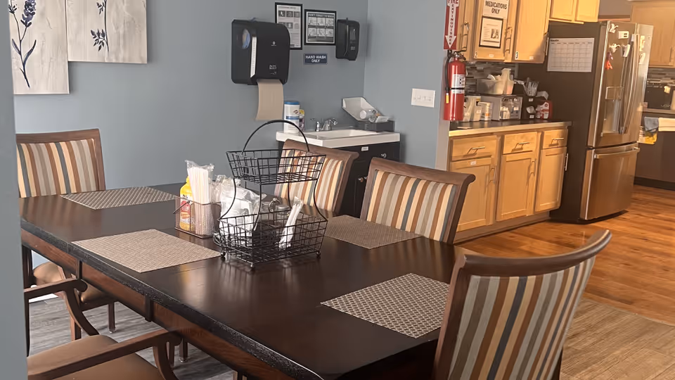 A shared dining area with a dark table, striped chairs, and a kitchenette in the background.