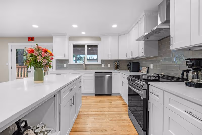 Bright modern kitchen with white cabinets, stainless appliances, and a flower centerpiece on the island.