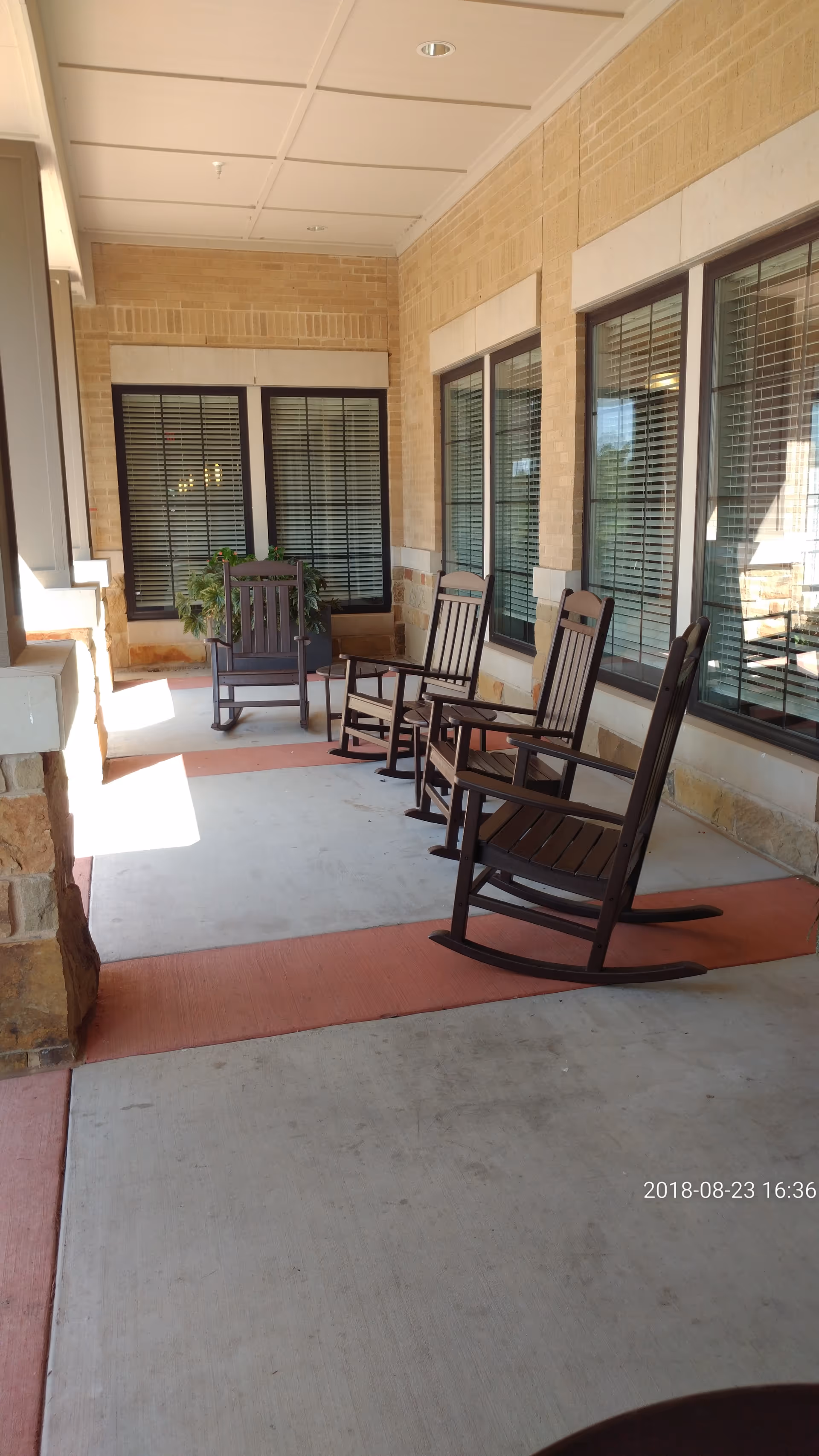 Covered outdoor porch with rocking chairs along a brick exterior.