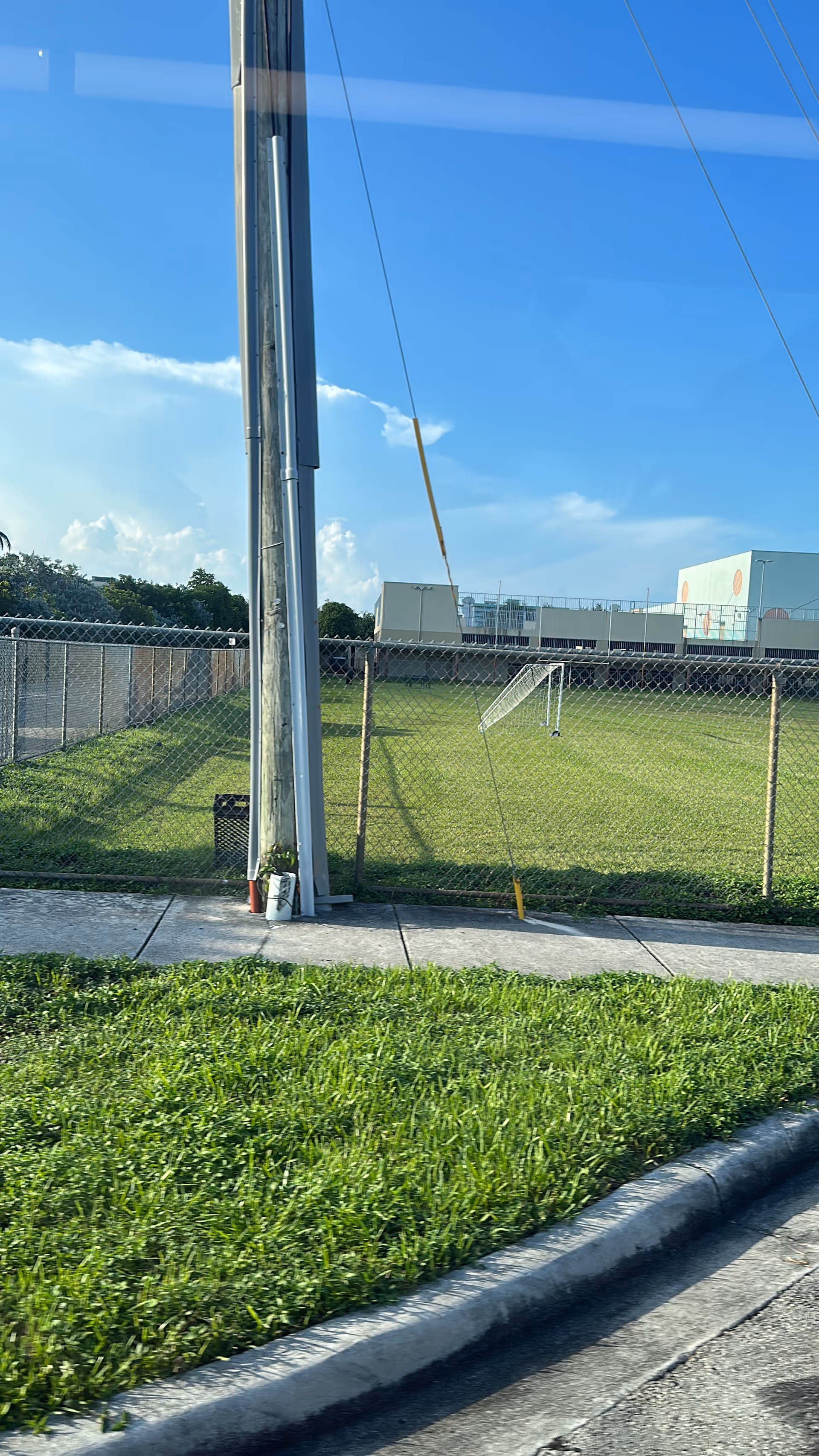 Outdoor view of a chain-link fence, pole, sidewalk, and grassy field.