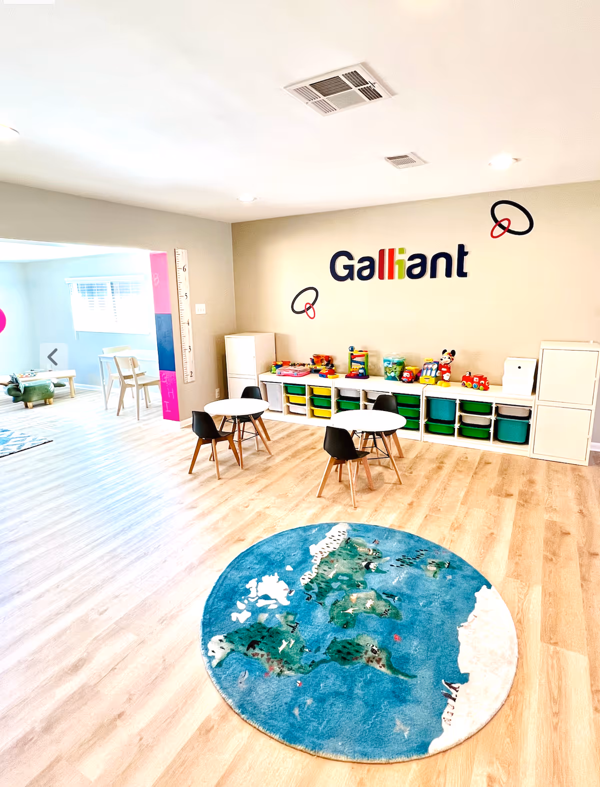 Bright children's play area with small tables, toys, storage cubbies, and a map rug.