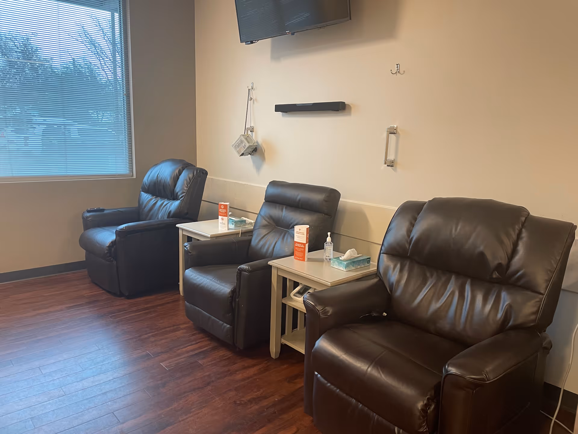 Three black leather lounge chairs with small tables in a neutral infusion center waiting area.