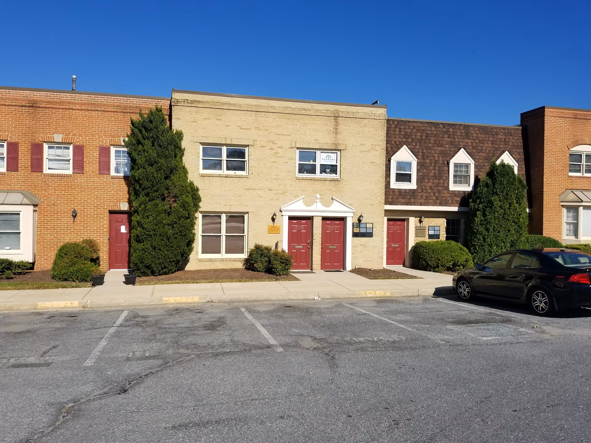 Exterior view of a senior living facility with red doors, shrubs, and a parked car.