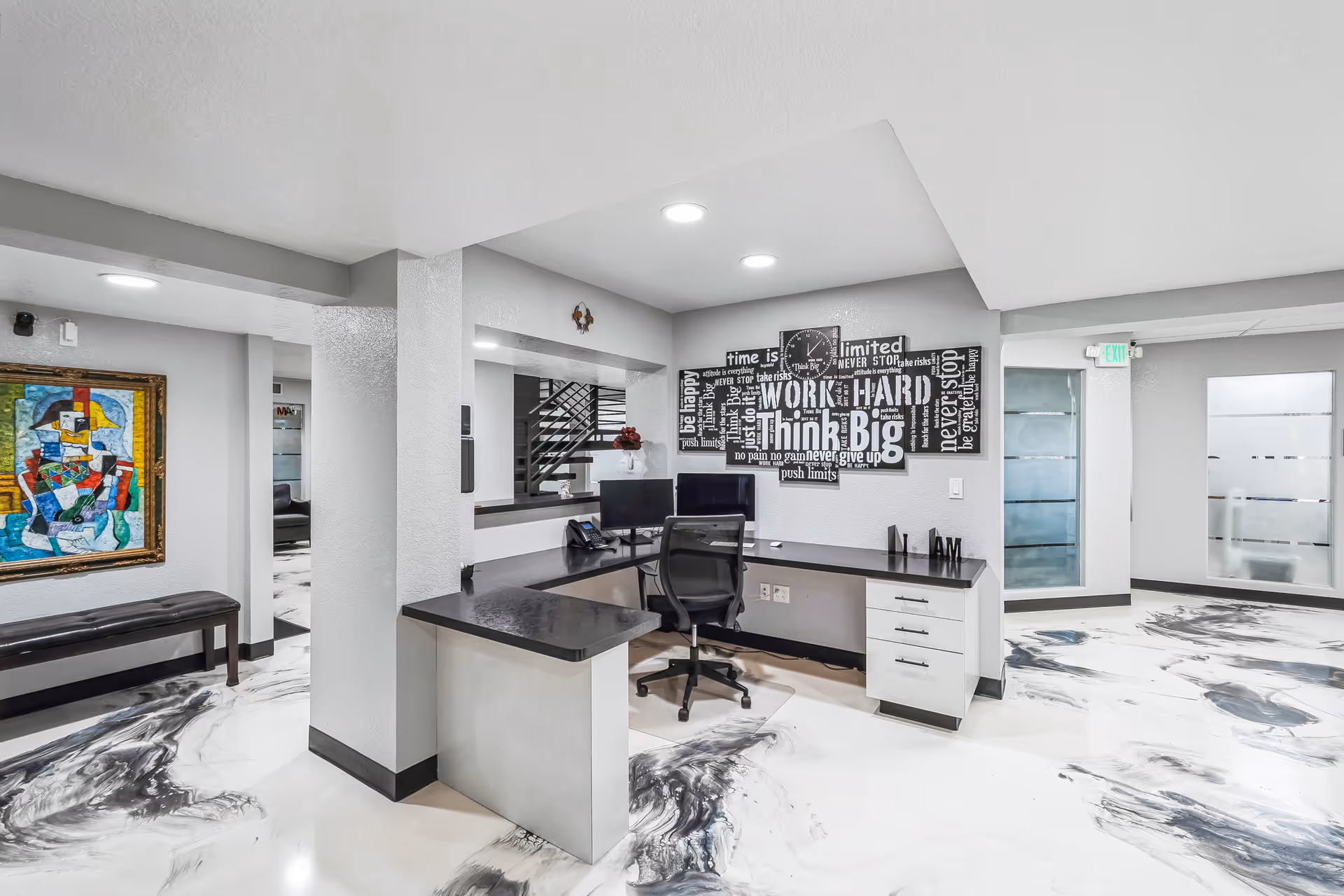 Modern reception desk in a bright lobby with marble floors, artwork, and seating.