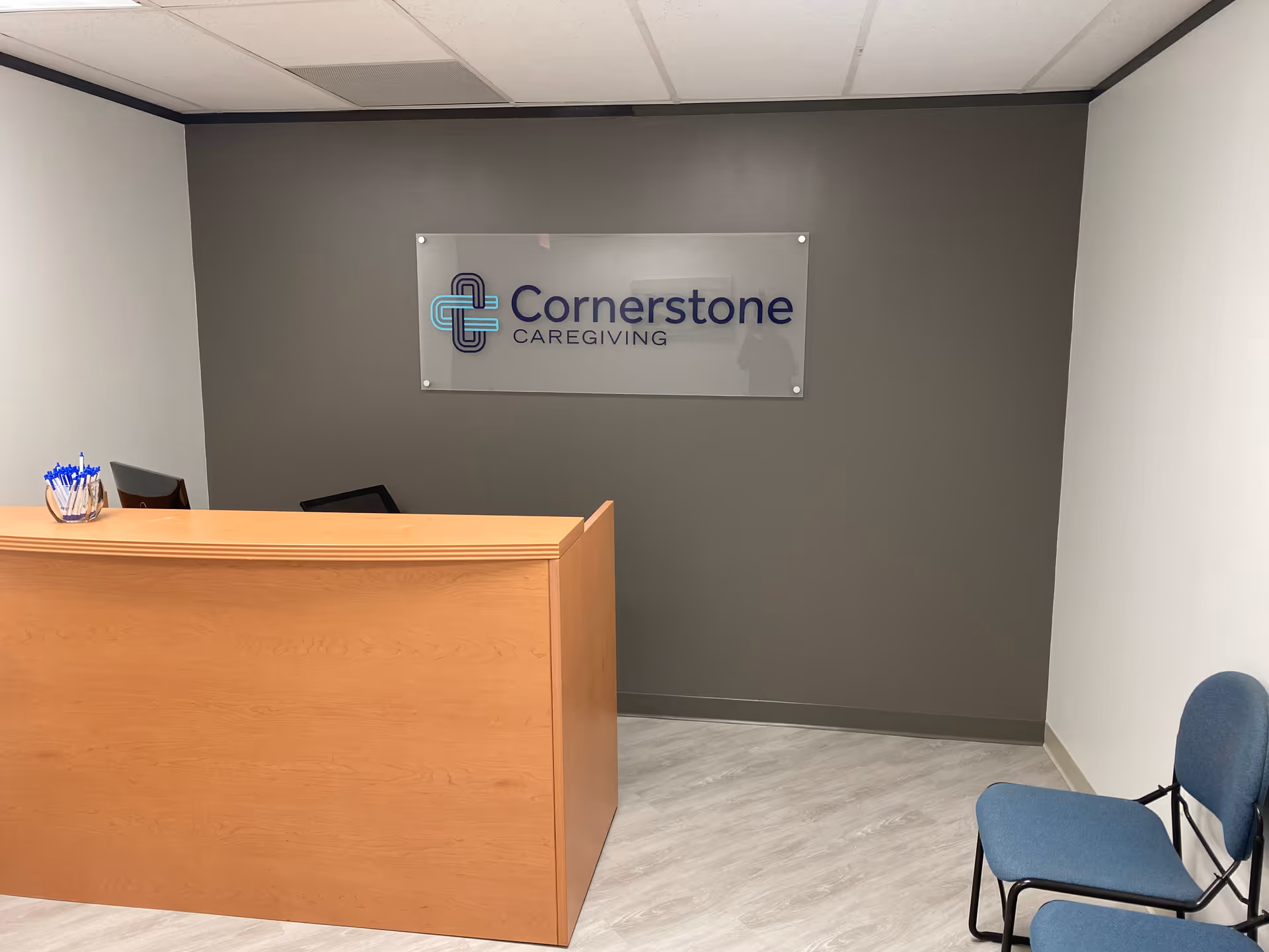 Reception desk against a gray wall with a Cornerstone Caregiving sign in a lobby.