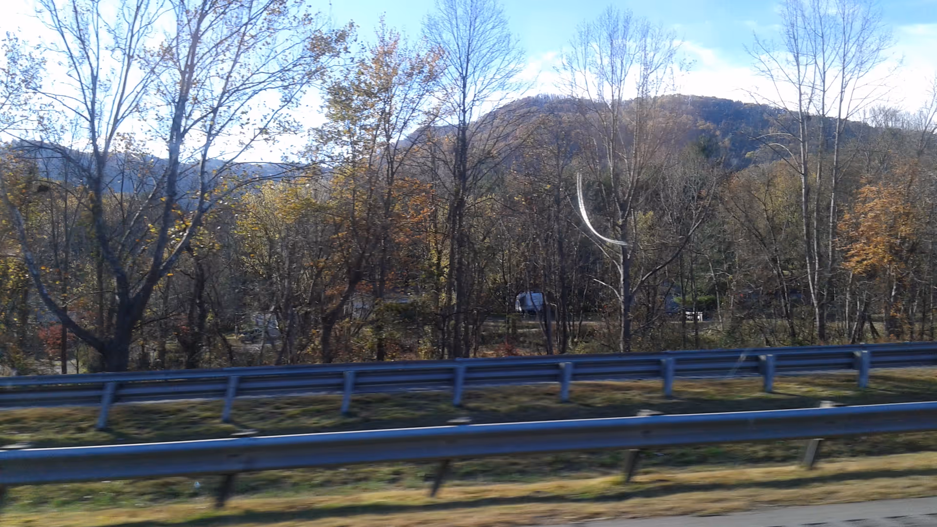 Roadside scene with guardrails, leafless trees, and distant hills.