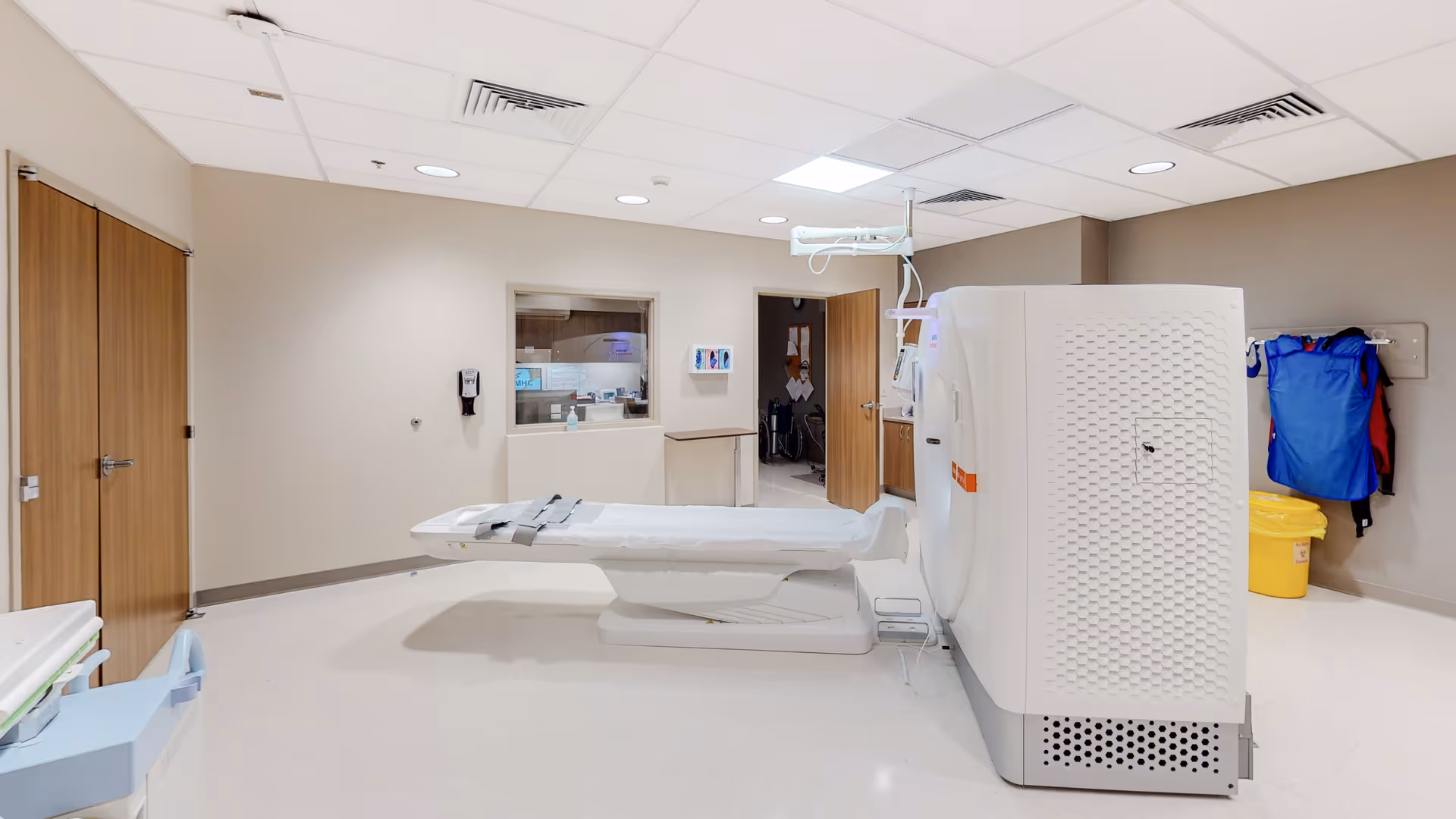 Medical imaging room with a CT scanner and patient bed in a sterile hospital setting.