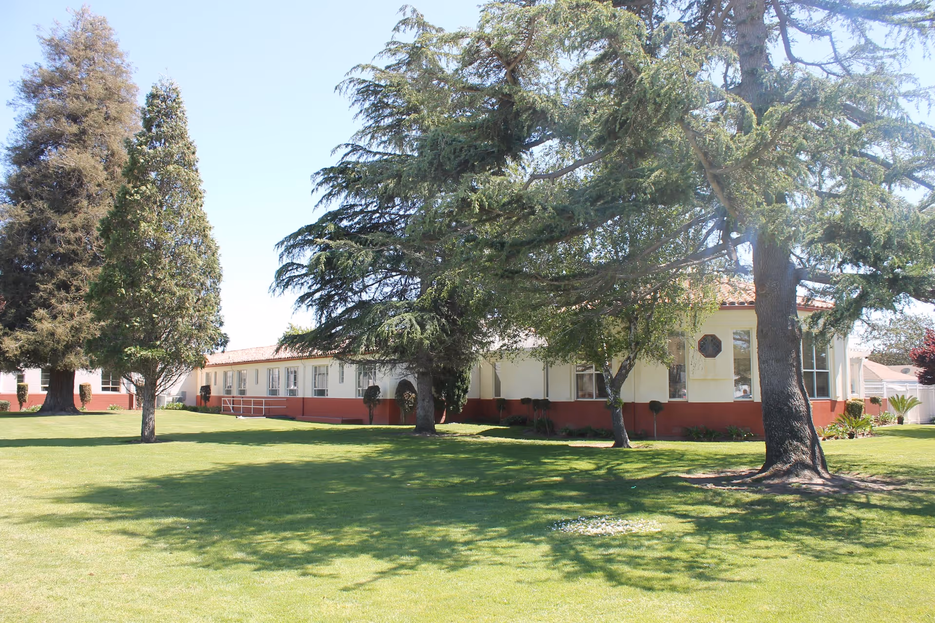 Exterior view of a single-story facility with white walls, red base, and trees.