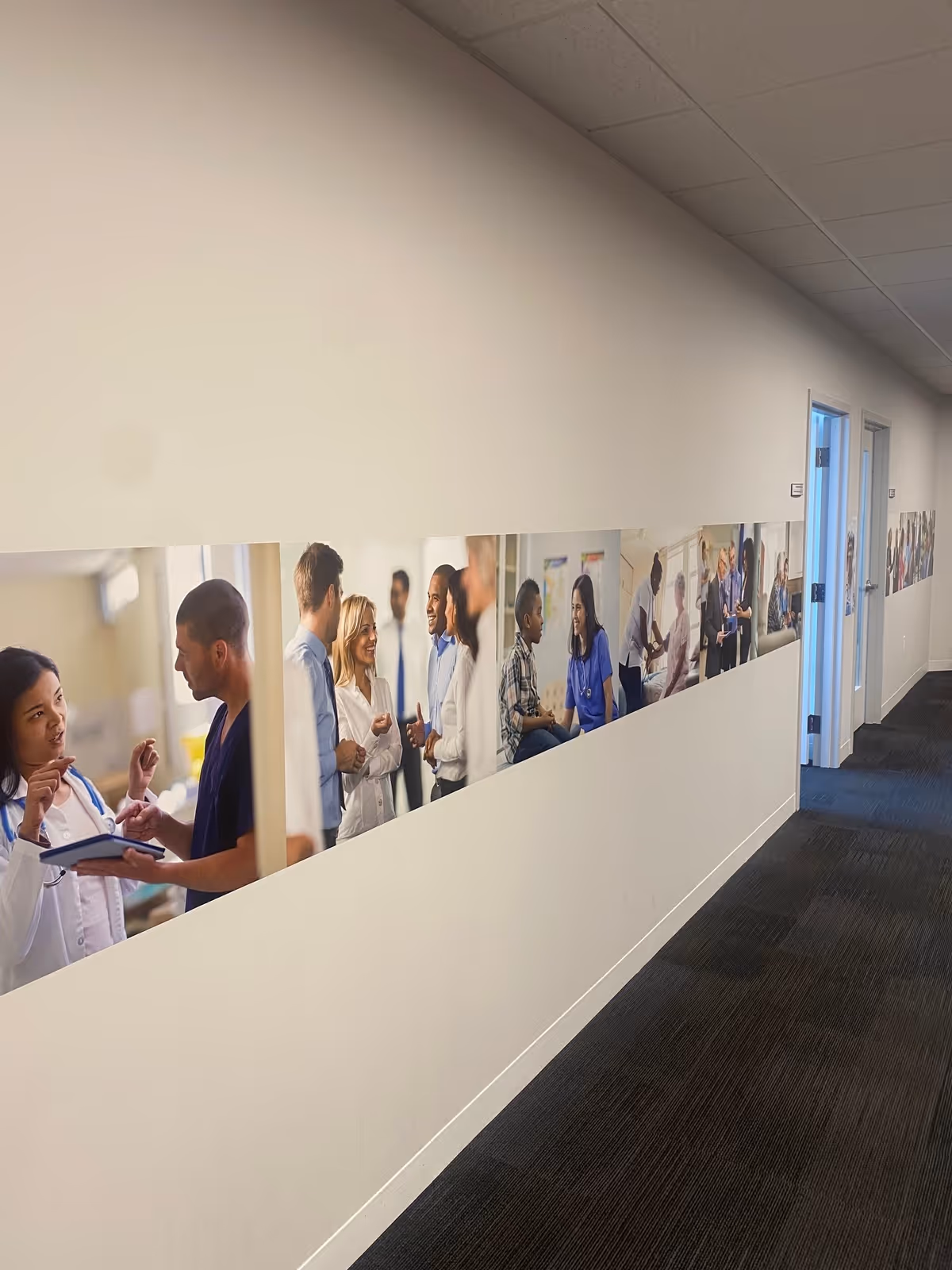 Interior corridor with a wall mural of medical staff photos and doorways.