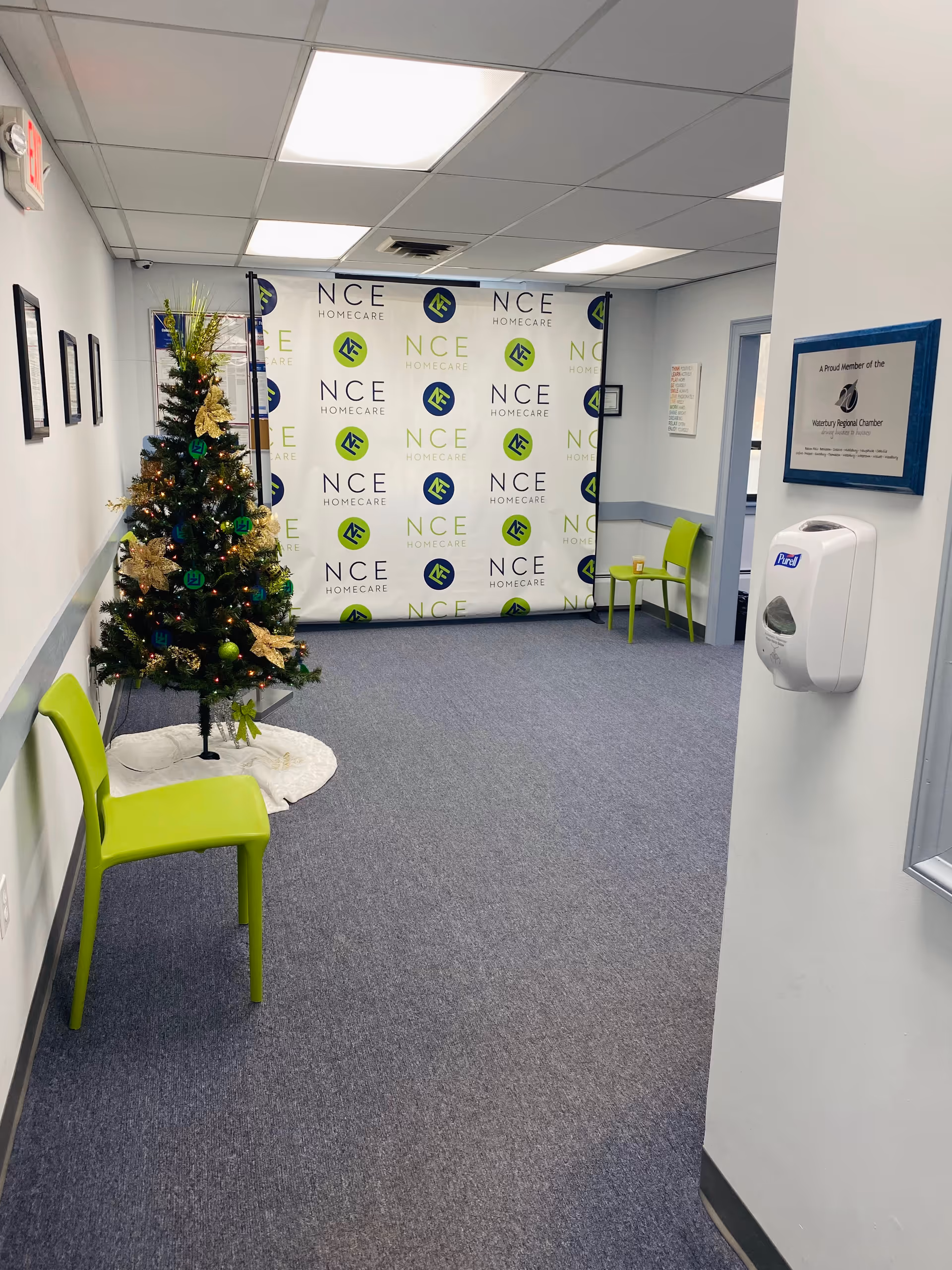 Interior hallway at NCE Homecare featuring a Christmas tree, green chairs, and a branded backdrop.