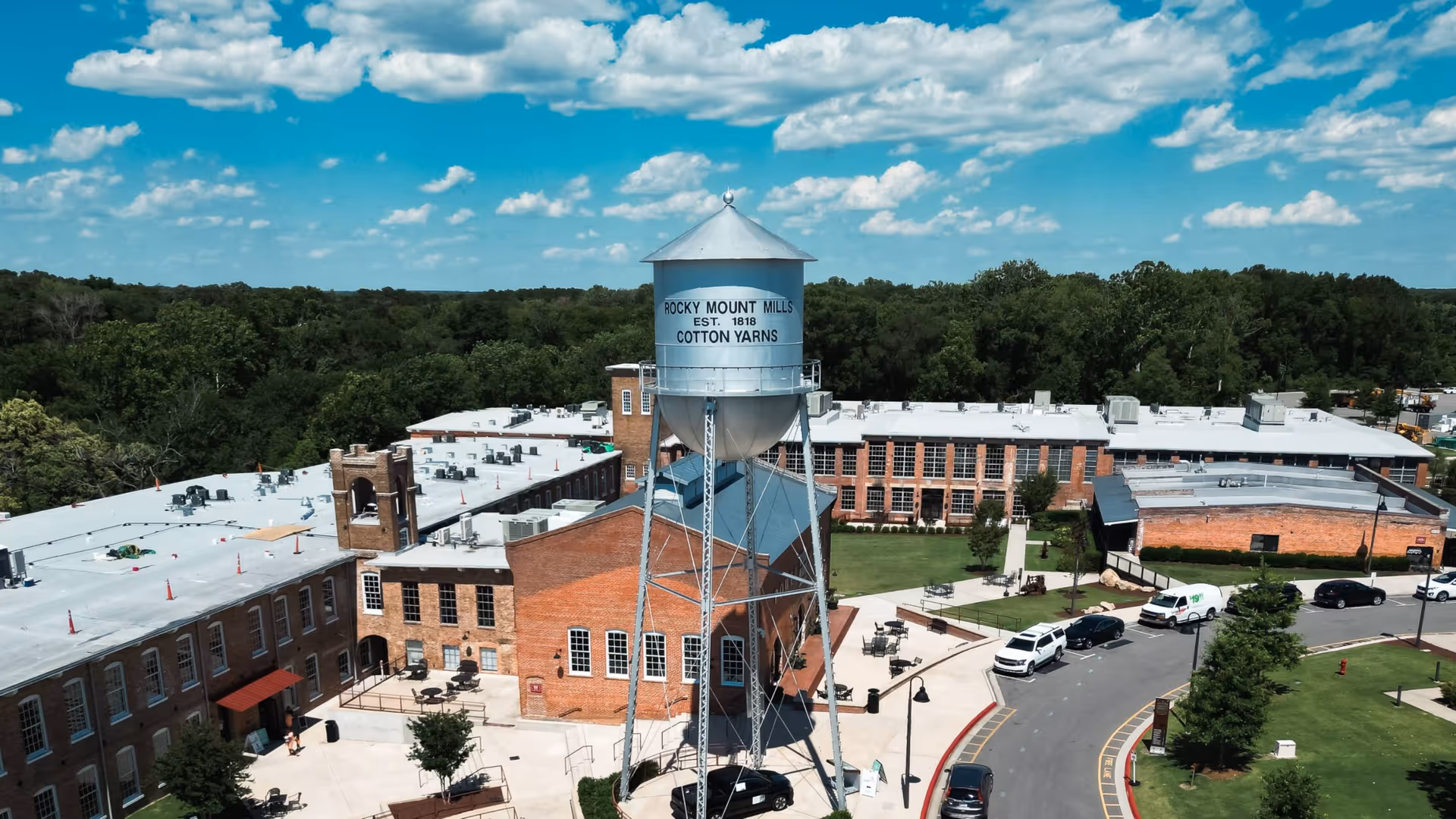 Aerial view of a brick campus with a tall water tower, curved road, and trees.