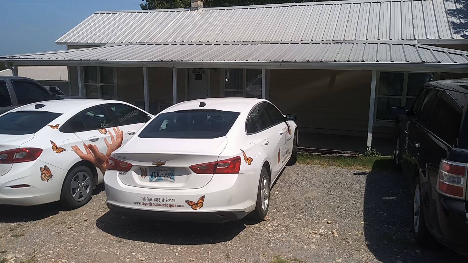 Exterior view of a single-story building with parked cars in front and a metal roof.