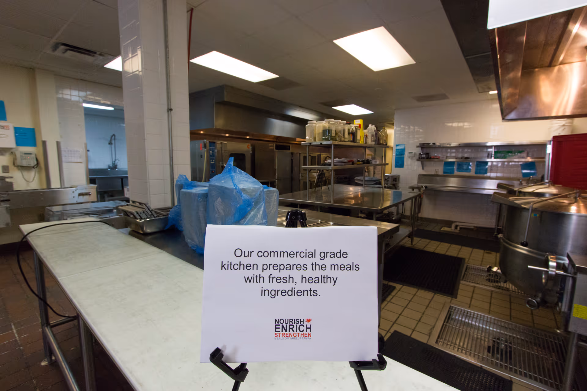 Industrial commercial kitchen with stainless steel equipment and a sign about fresh ingredients.