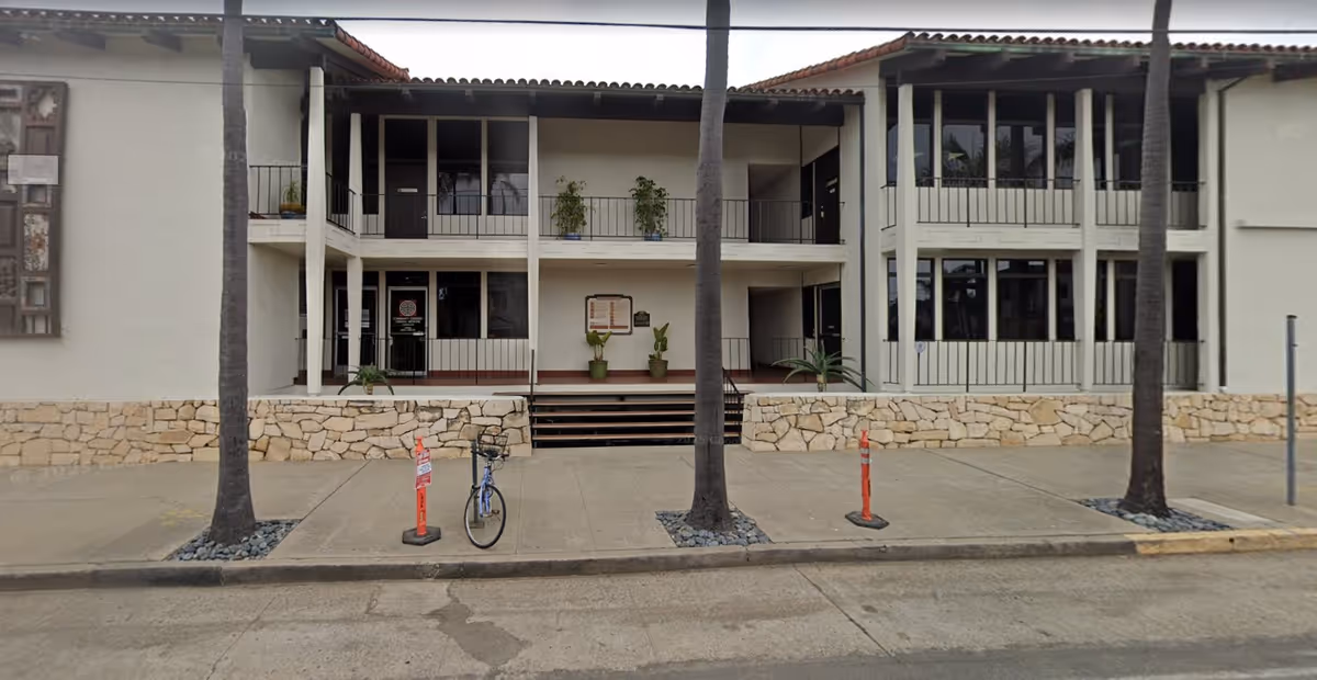 Two-story Senior Helpers building facade with stone base, palm trees, and bicycles outside.