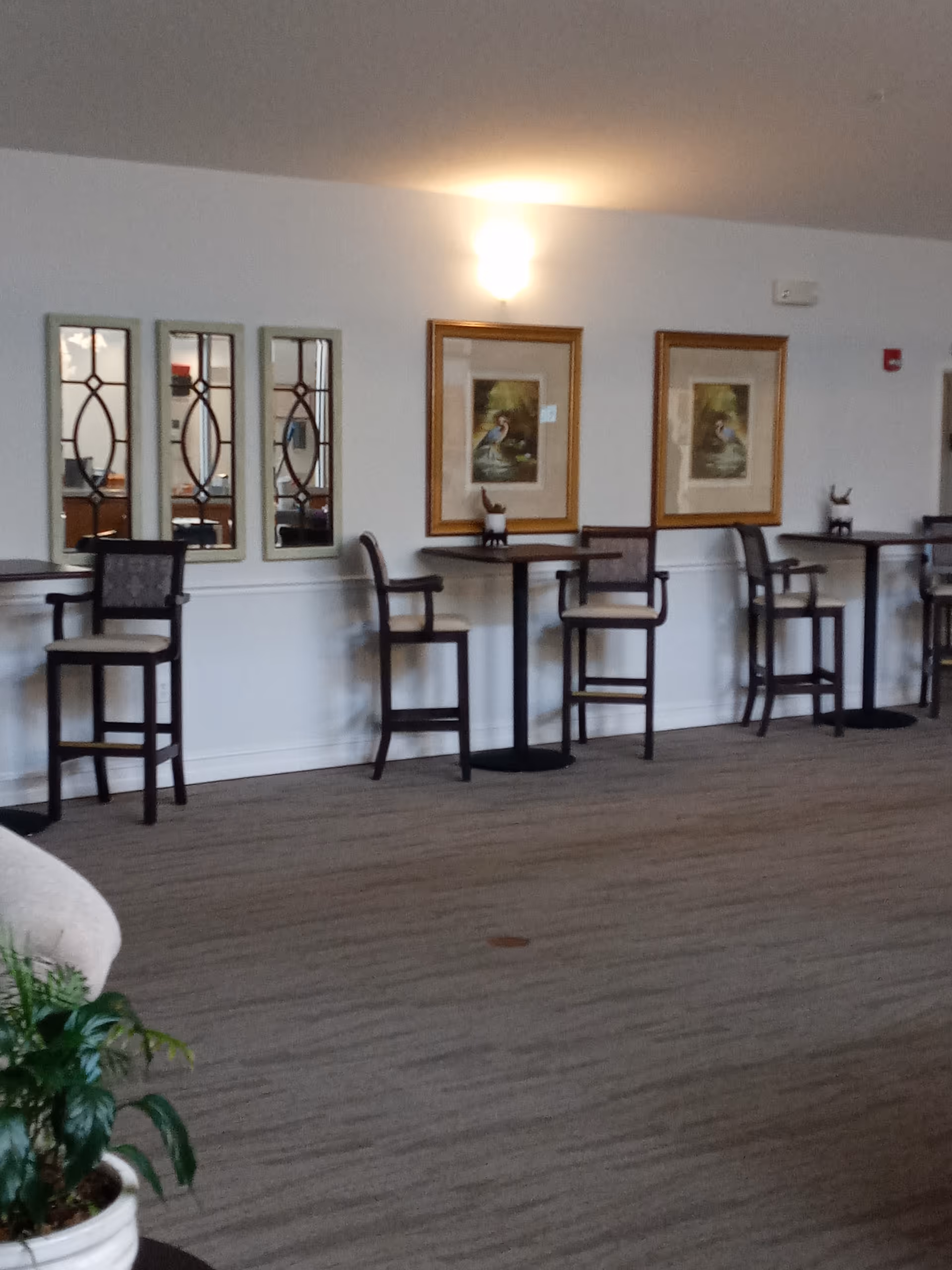 Interior lounge area with high tables, chairs, framed art, and a potted plant.