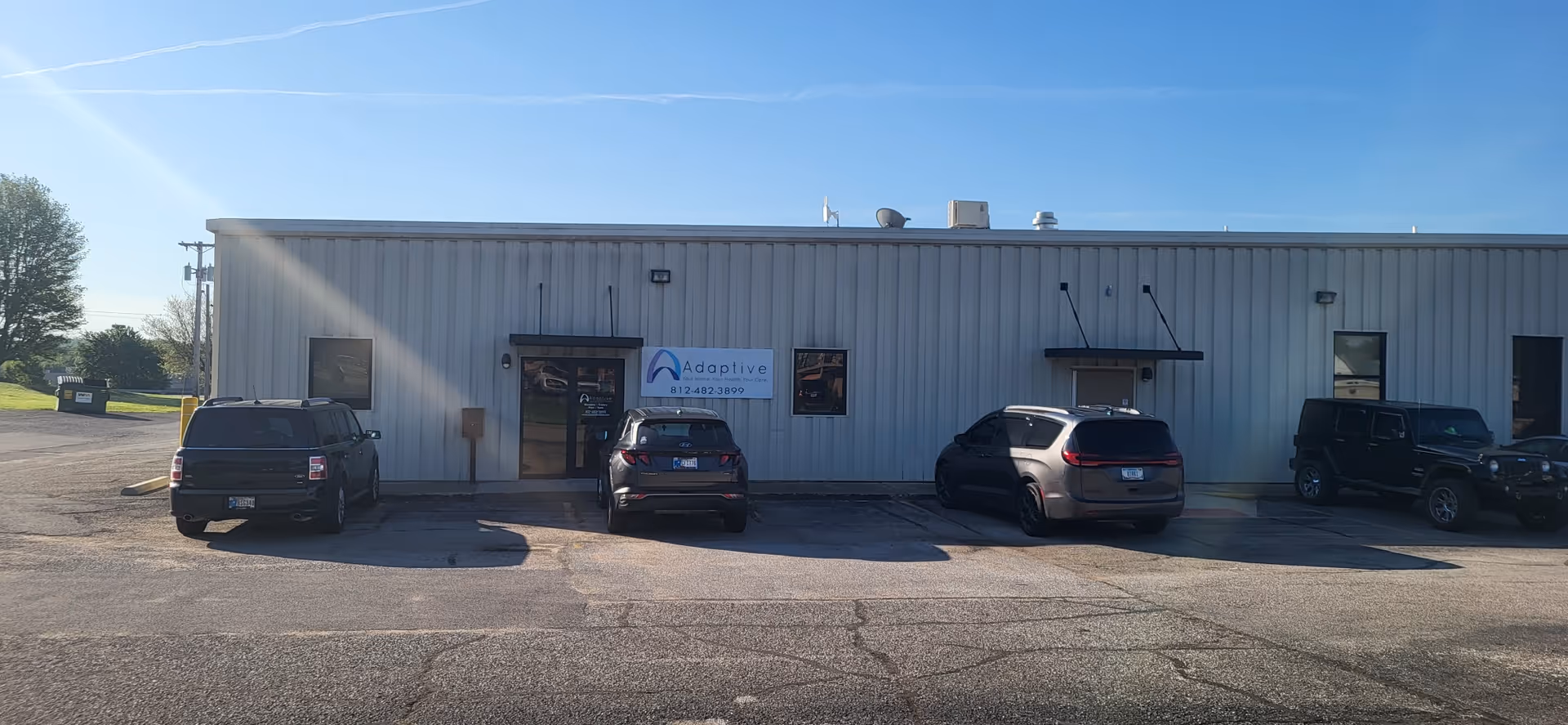 Front view of a metal-clad building with a sign and several parked cars.