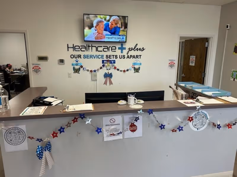 Reception desk inside a healthcare facility with a wall-mounted Healthcare Plus sign.