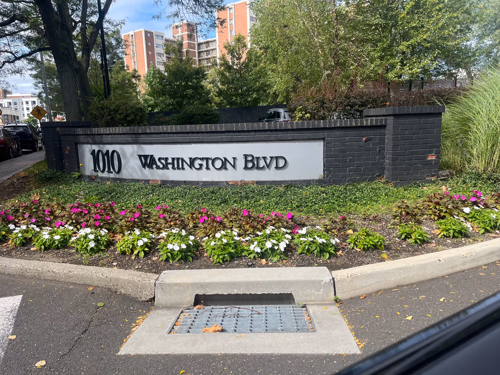 A brick sign displays 1010 Washington Blvd with flowers and trees nearby.