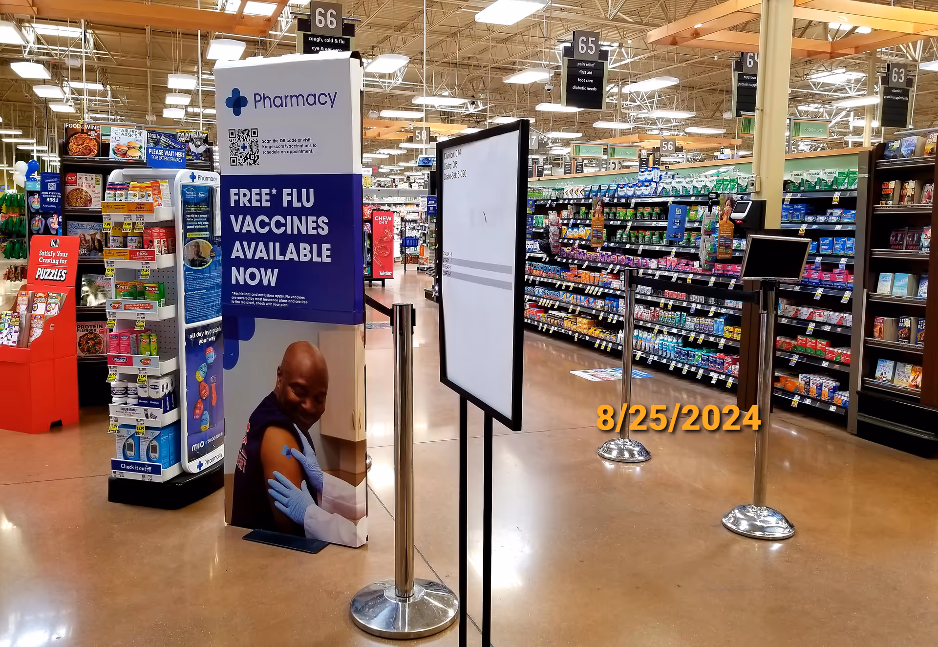 Inside a Kroger store, pharmacy sign and vaccine ad amid aisles and checkout stands.
