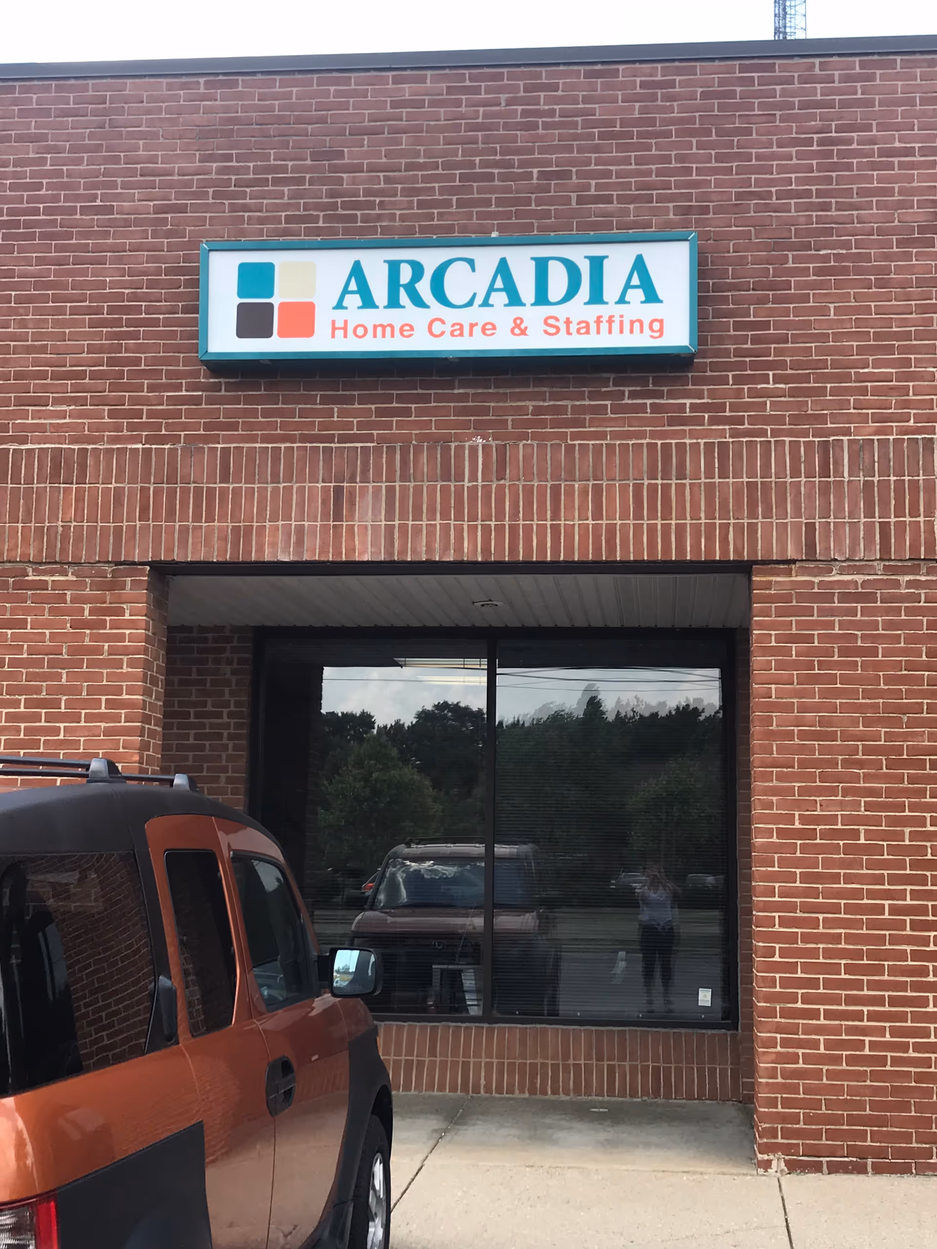 Arcadia Home Care & Staffing storefront sign on brick building with a parked orange SUV.