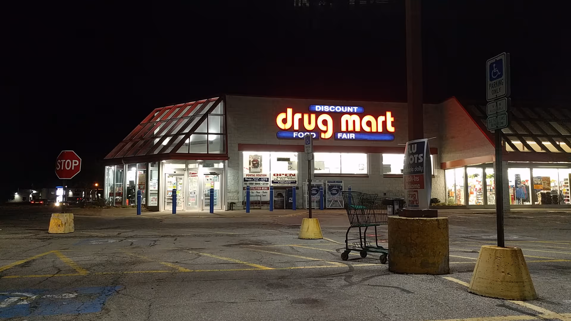 Nighttime exterior of a Discount Drug Mart storefront with illuminated sign and empty parking lot.