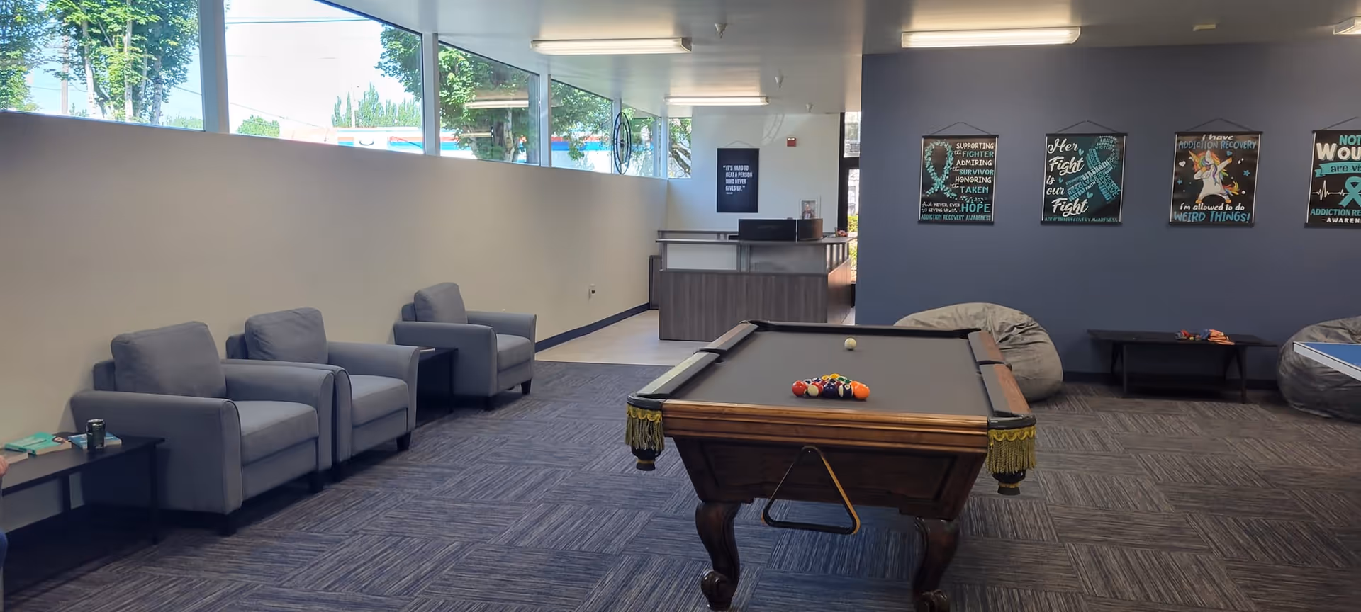 Indoor common lounge with a billiards table, gray chairs, bean bags, and posters.