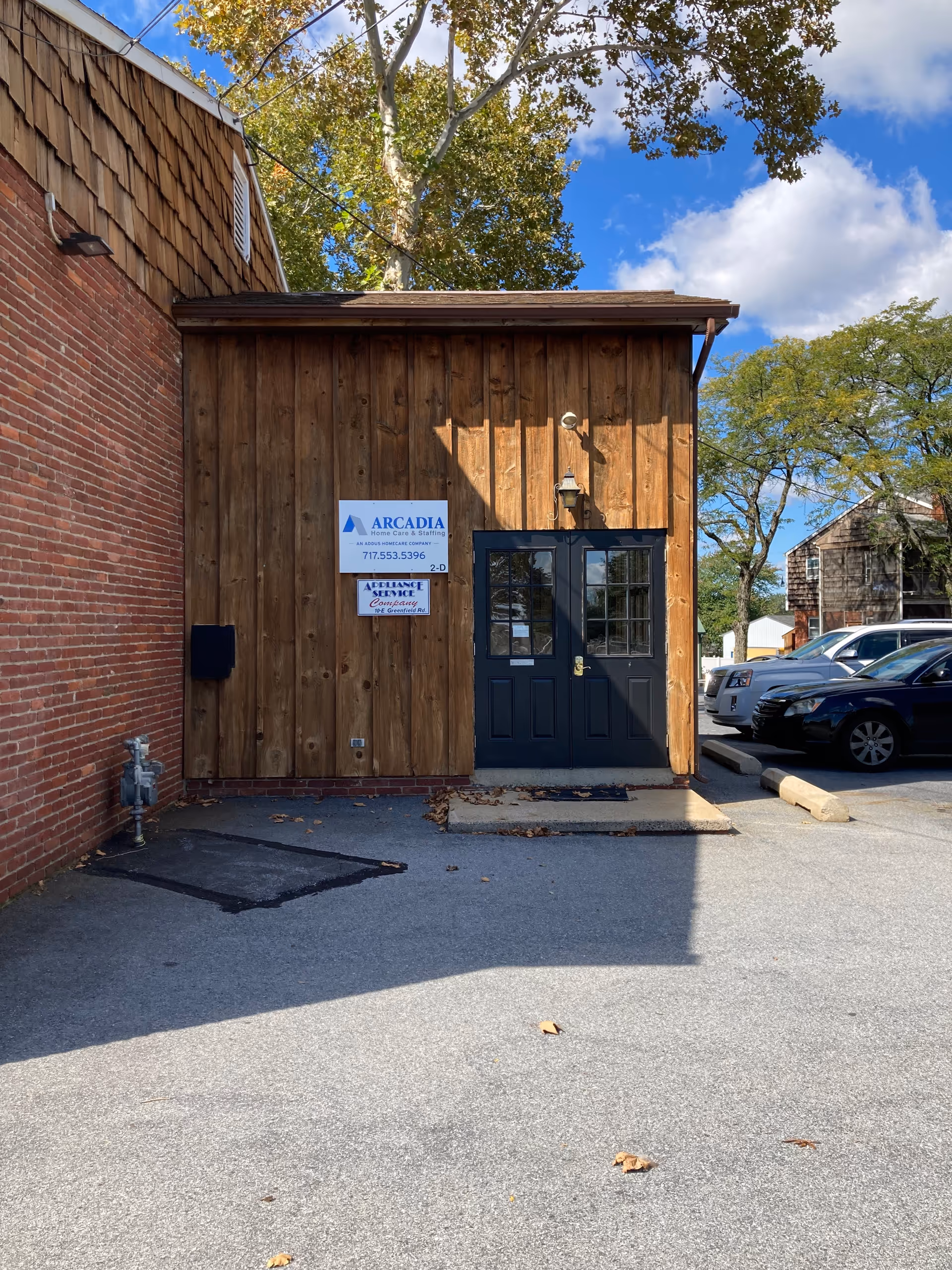 A wooden exterior front entrance to Arcadia Home Care & Staffing with signage and parked cars.