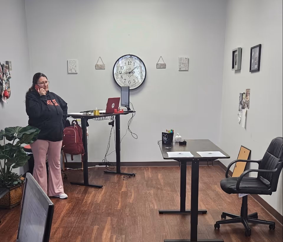 A staff member on a phone stands beside a standing desk in a small office.
