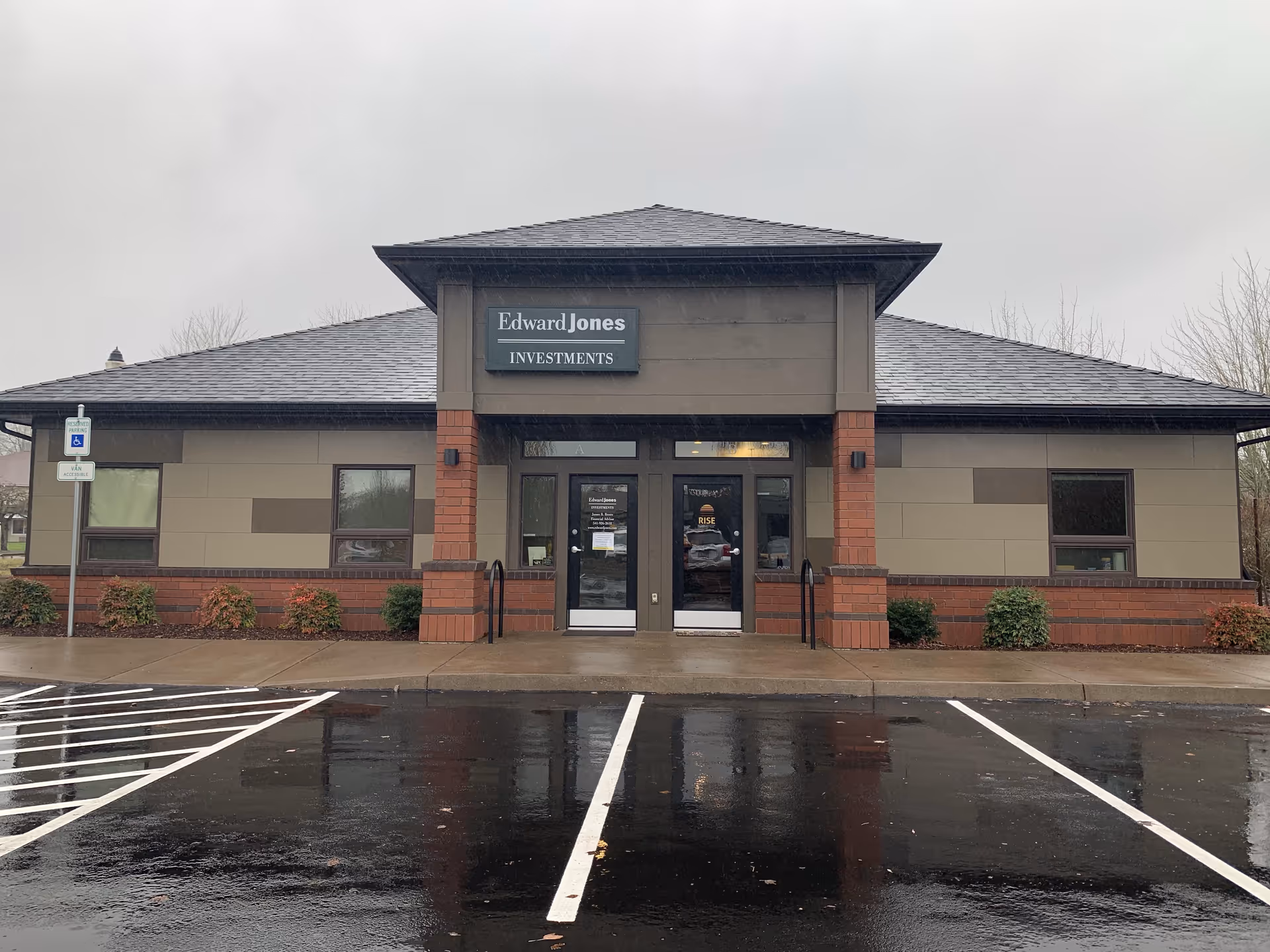 Facade of a single-story building with a sign and glass entrance, parking lot in front.