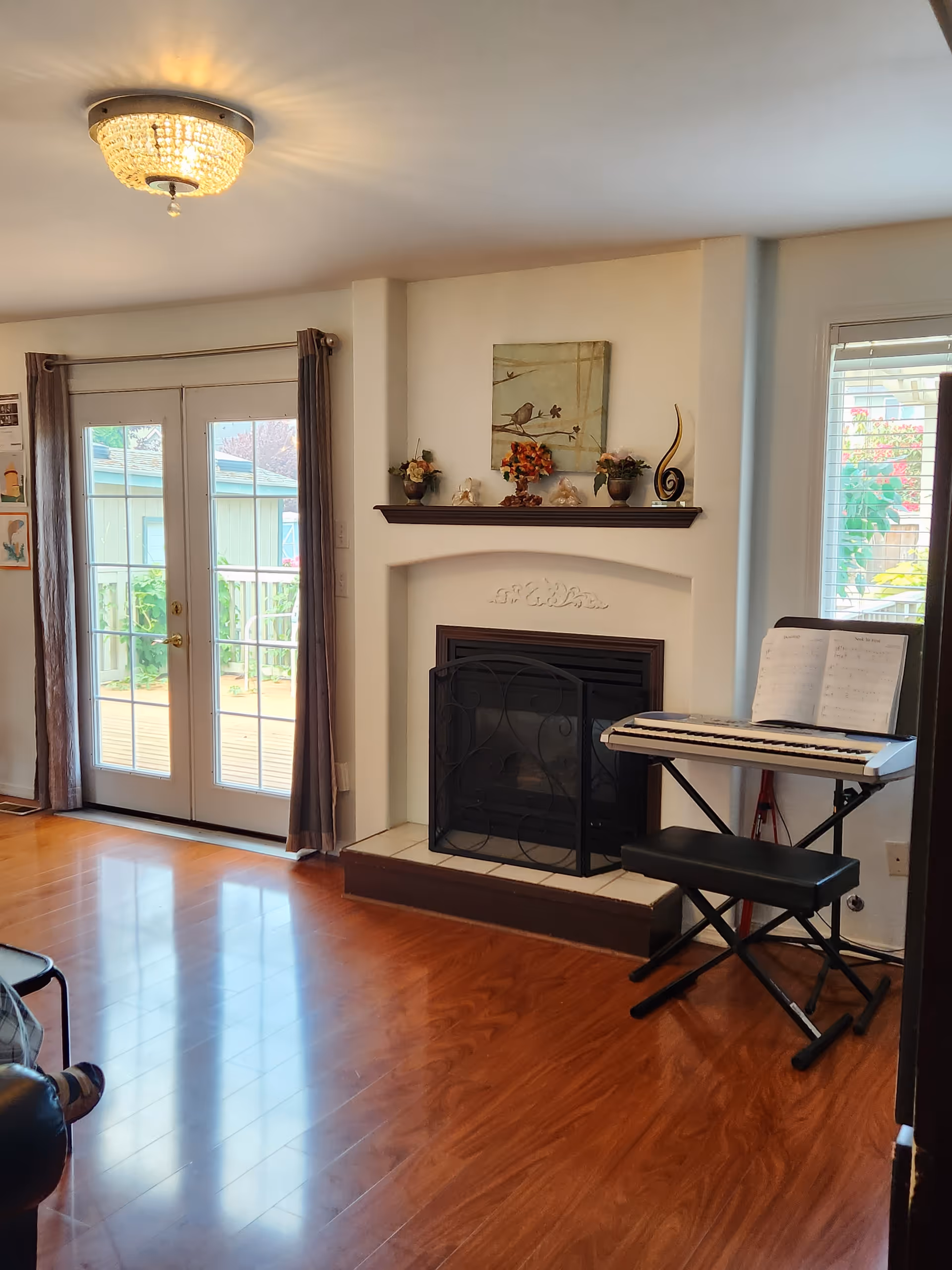 Living room with a fireplace, keyboard, French doors, and wooden floors.