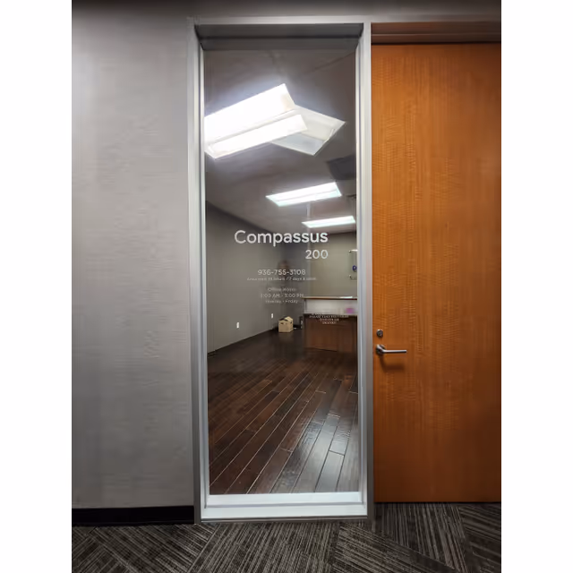 Glass door with Compassus branding opens to a wood-floored interior hallway.