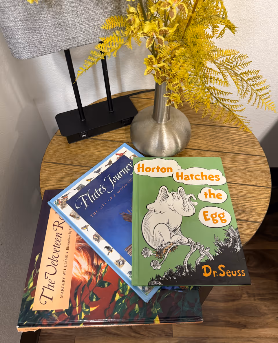 Wood table with a lamp, yellow fern vase, and children's books including Horton Hatches the Egg.