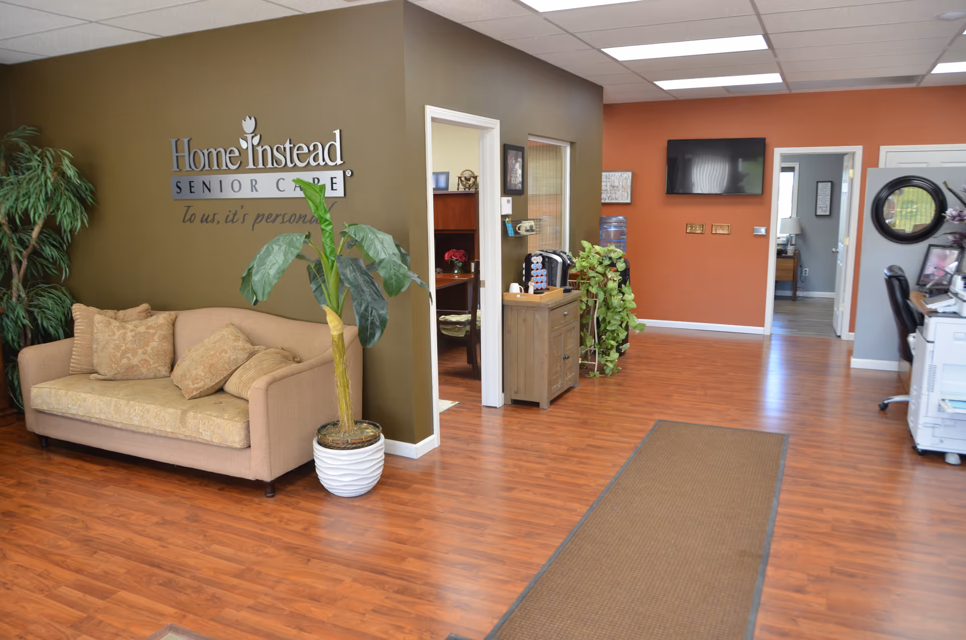 Reception area of Home Instead Senior Care with sofa, plants, and wood-toned flooring.