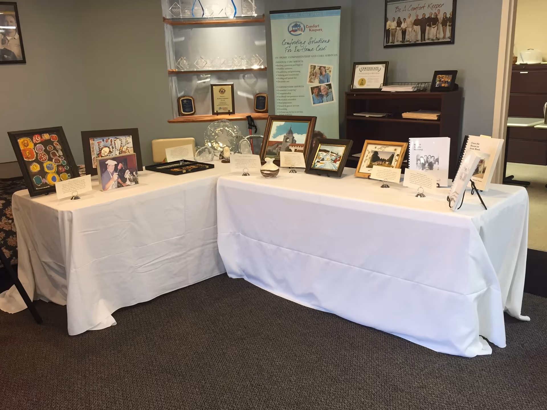 Two white-clothed display tables with framed photos and plaques in a conference room.