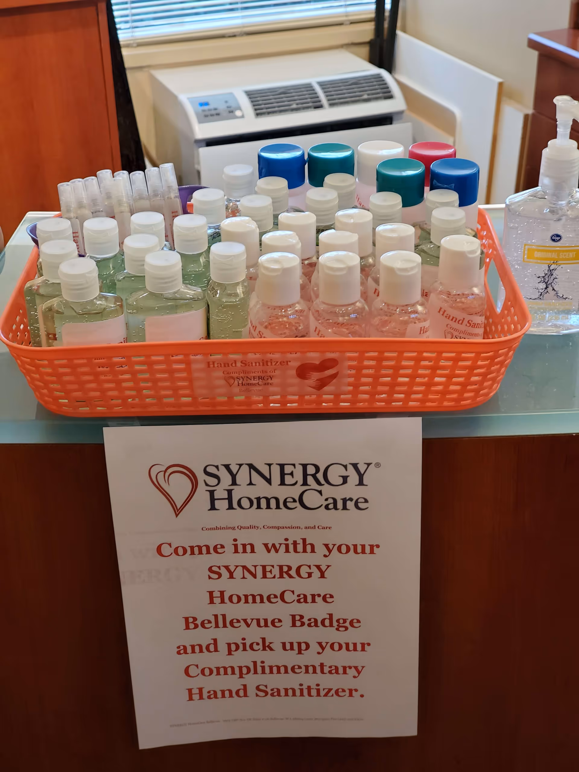 Orange basket filled with assorted hand sanitizers on a counter beside a Synergy HomeCare sign