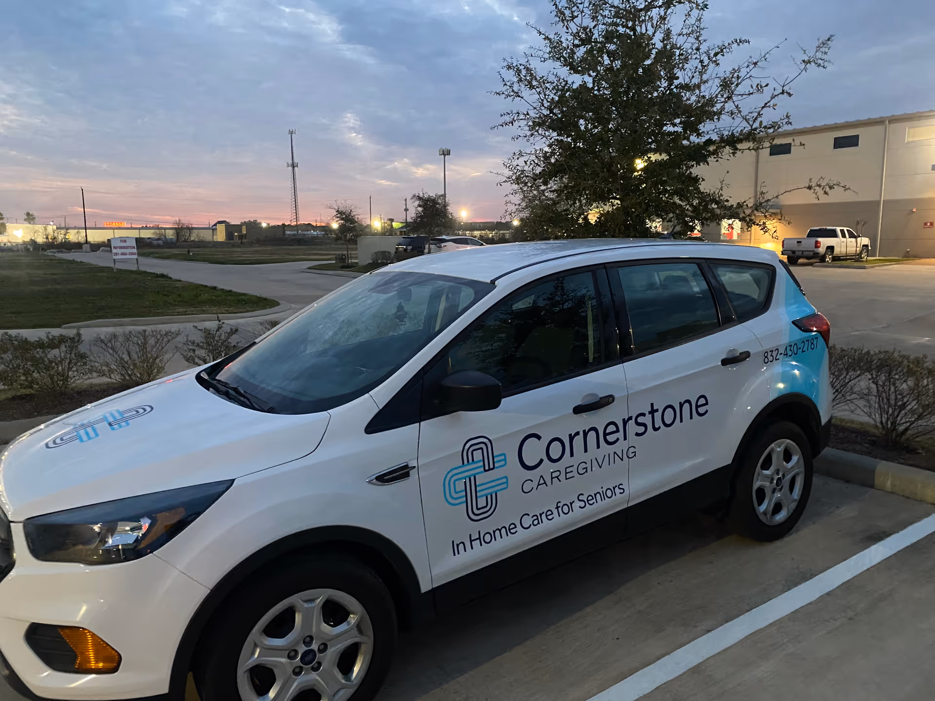 White Cornerstone Caregiving vehicle parked in a lot beside a building at dusk.