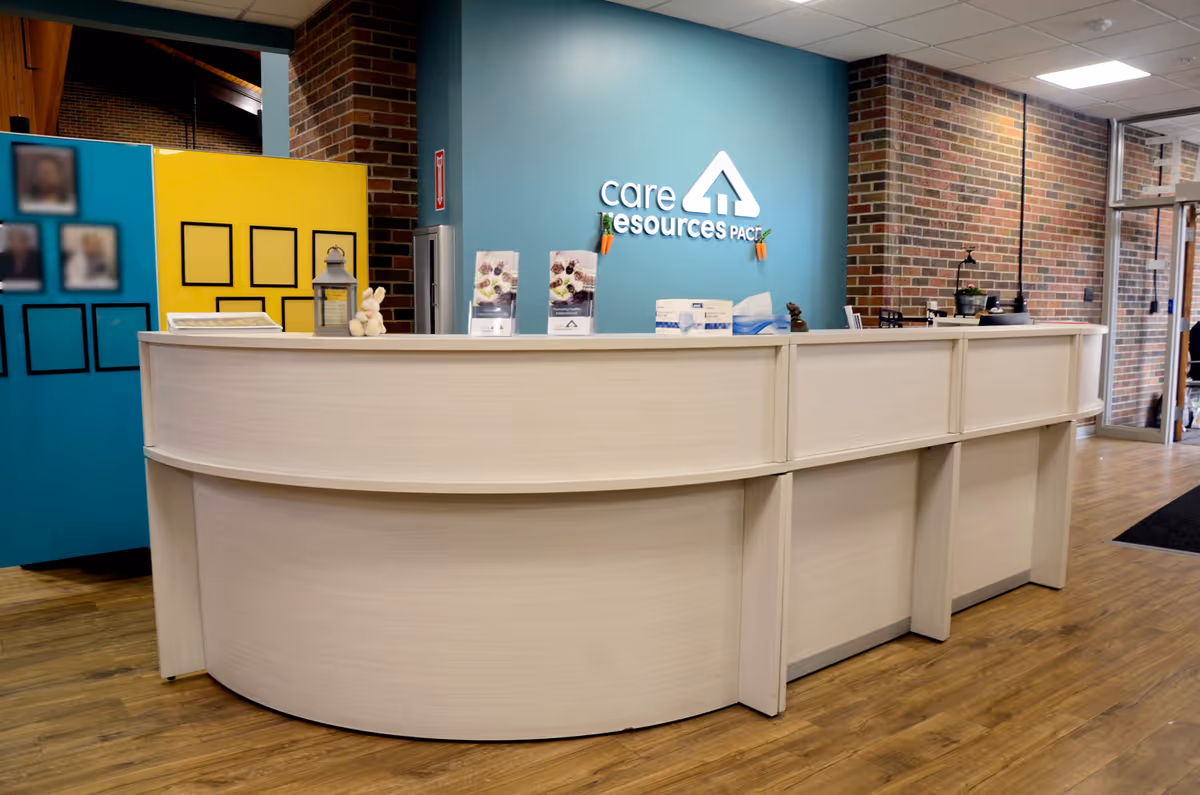 Curved white reception desk in a brick-walled lobby with a teal Care Resources – PACE sign.