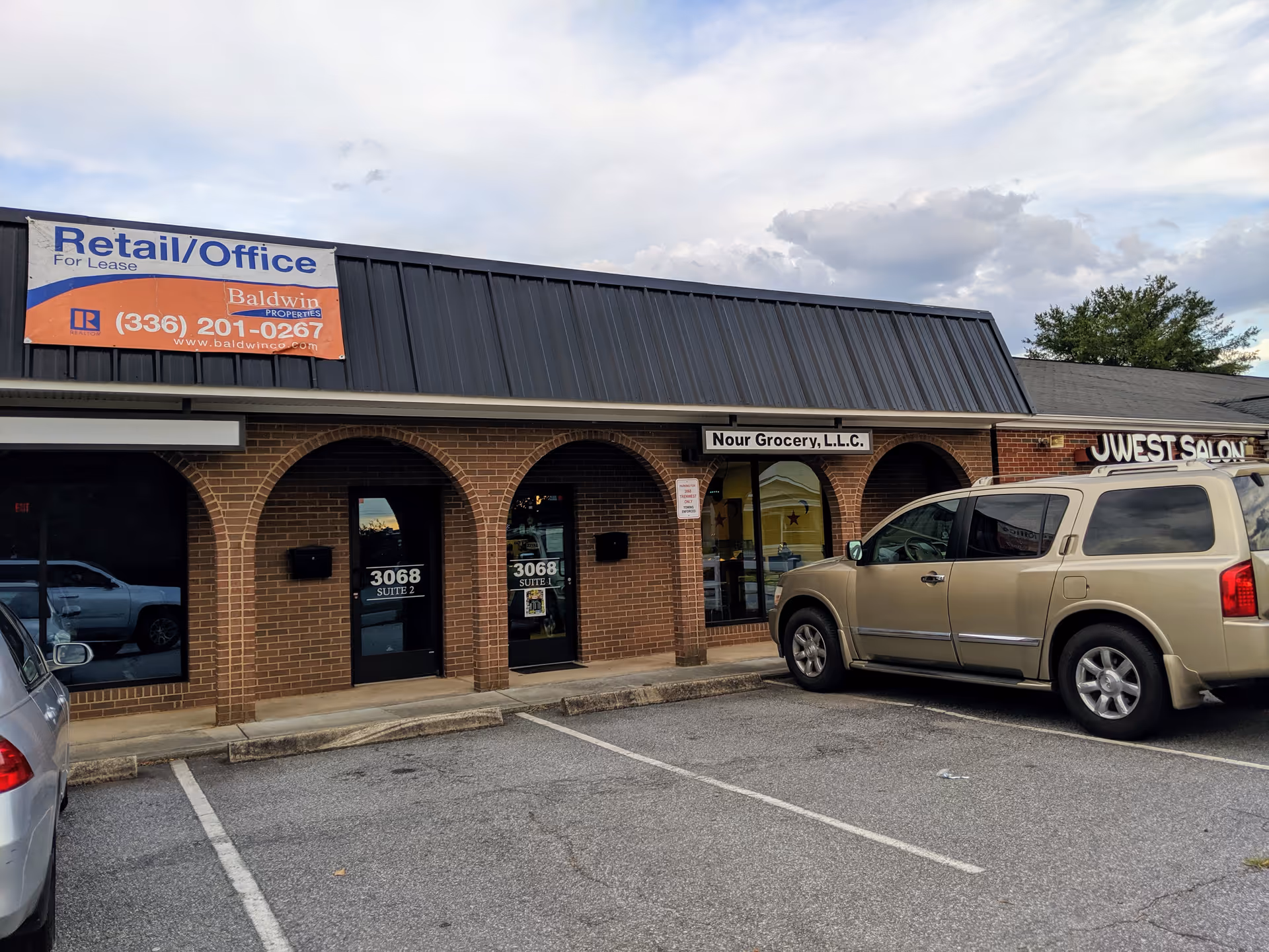 Exterior view of brick storefronts with arched entrances and parked vehicles.